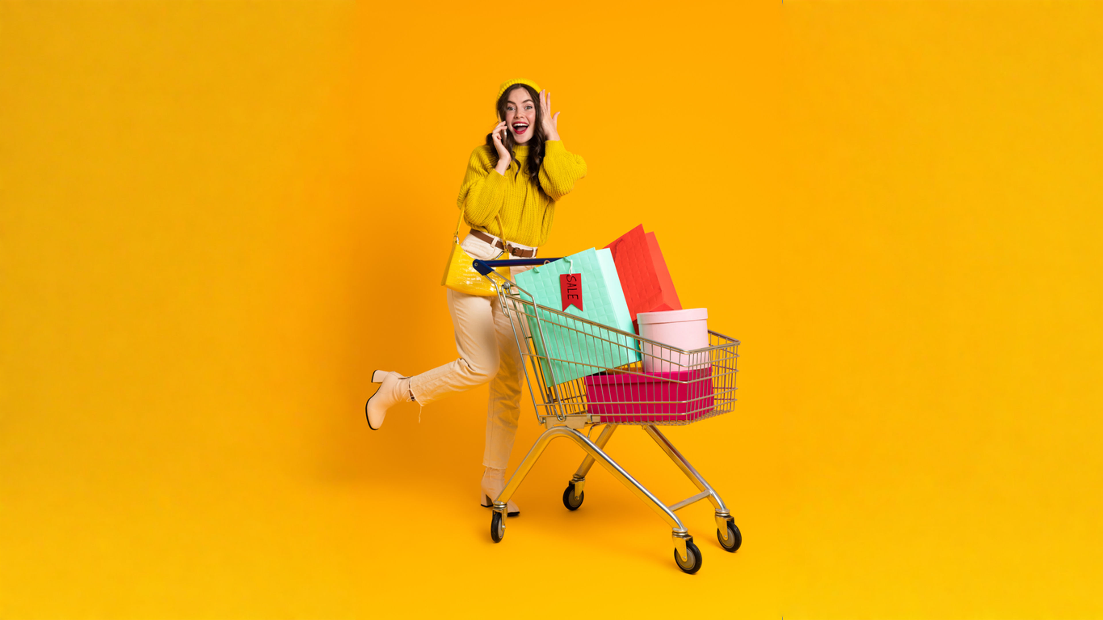 Excited woman talking on cellphone while posing with shopping cart.