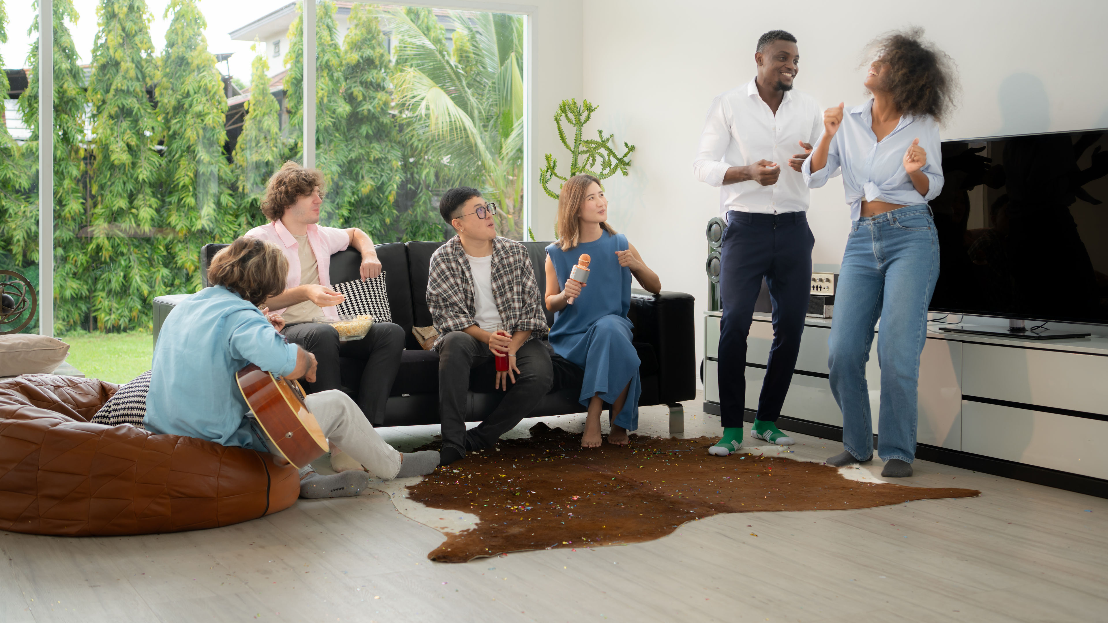 Group of multiethnic friends having fun at party by playing guitar, singing and dance together at home. 