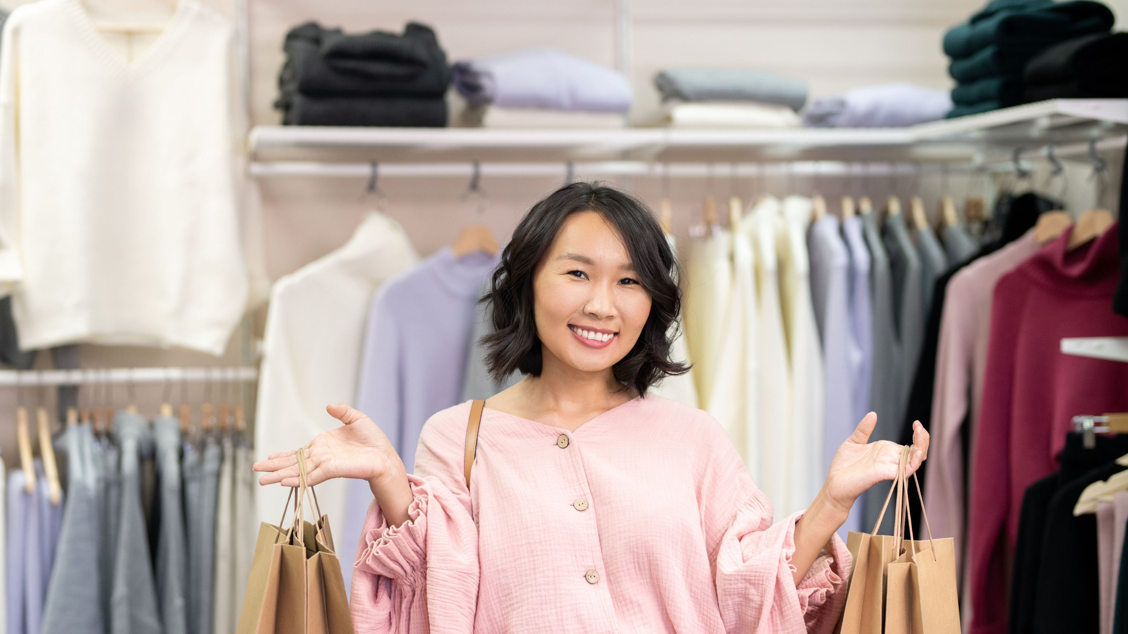 Young cheerful female in smart casualwear holding big paper bags in clothing store.