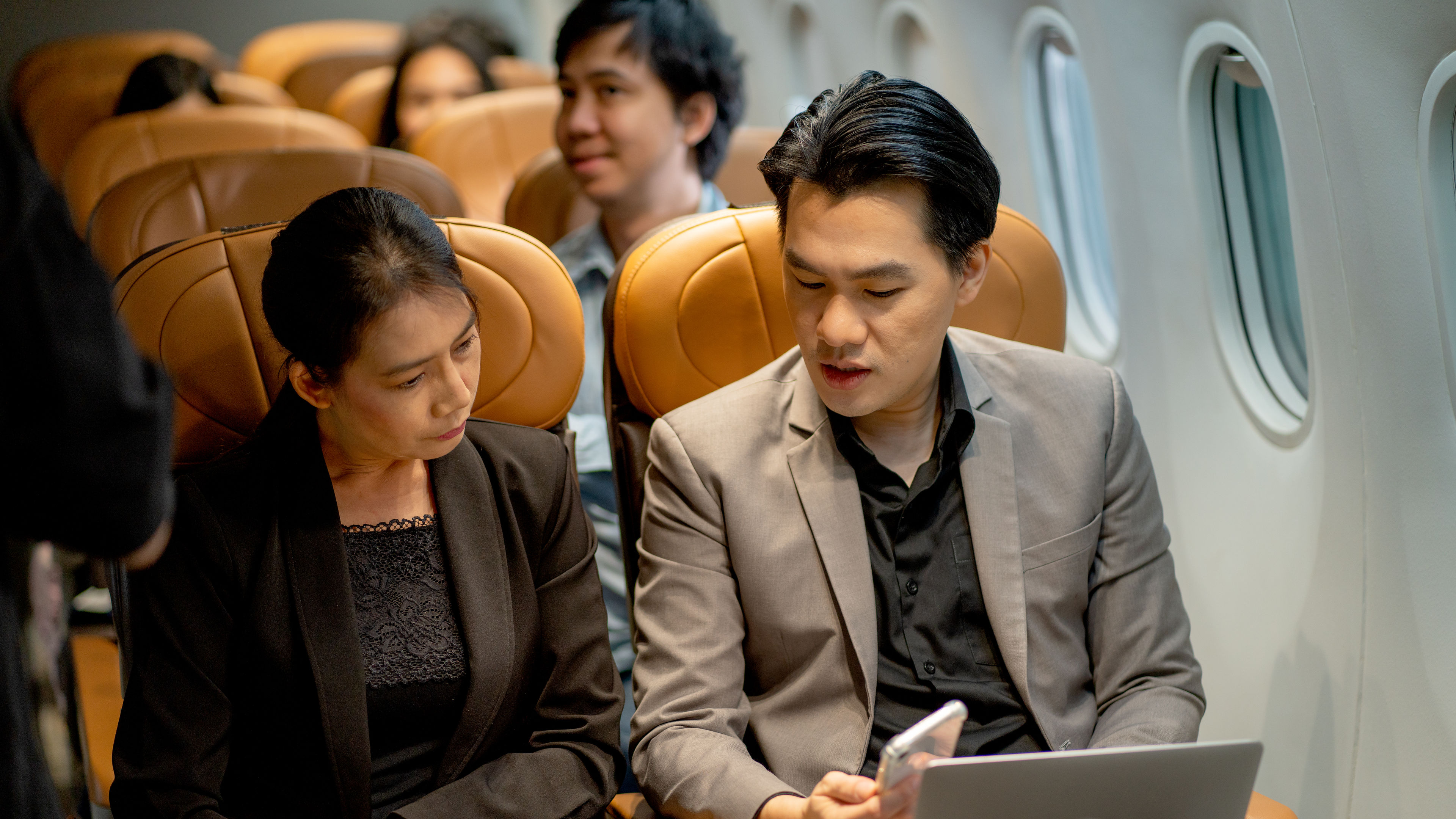 Businessperson gamitin ang laptop at ipakita ang data sa kanyang mobile phone sa katrabaho sa panahon ng fly with airplane. 