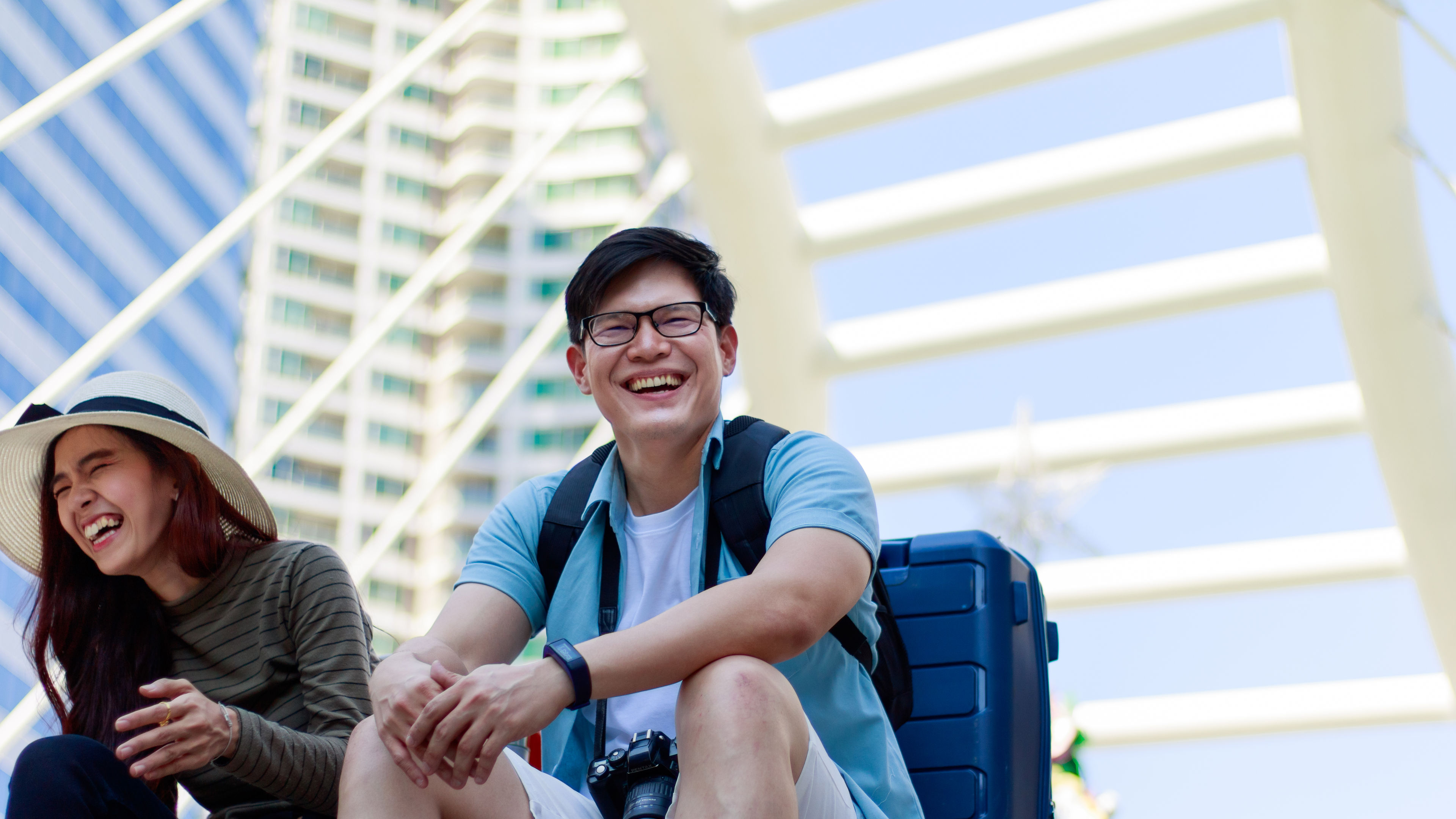 A cheerful man and women sitting with tourist bags and camera in hand.