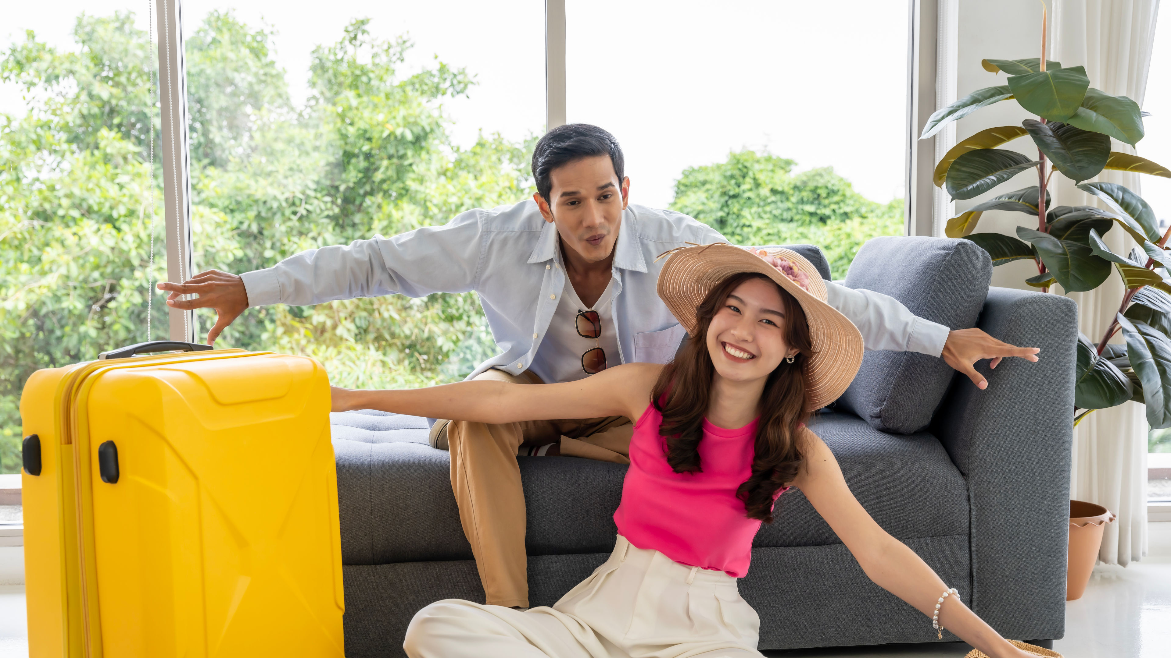 A Happy Asian couple posing together beside a yellow trolley in a hotel room.