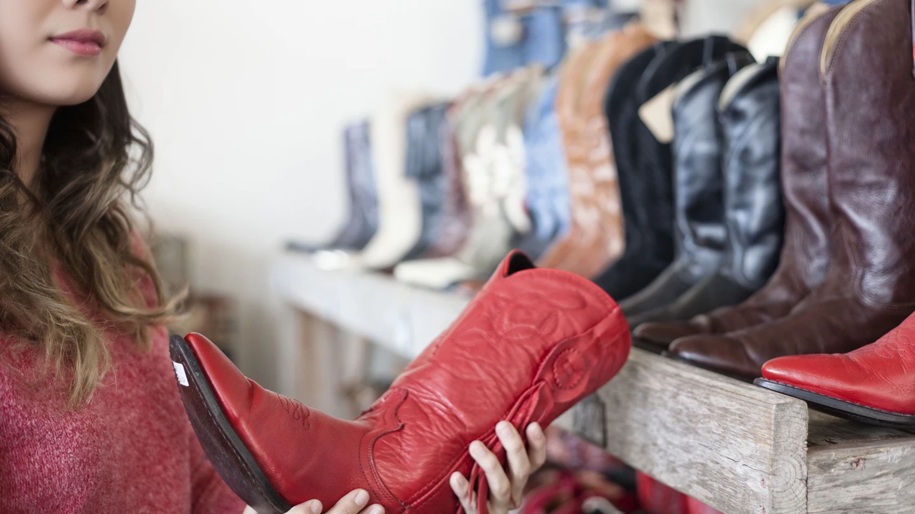 An Asian woman looking at boots for sale in a store.