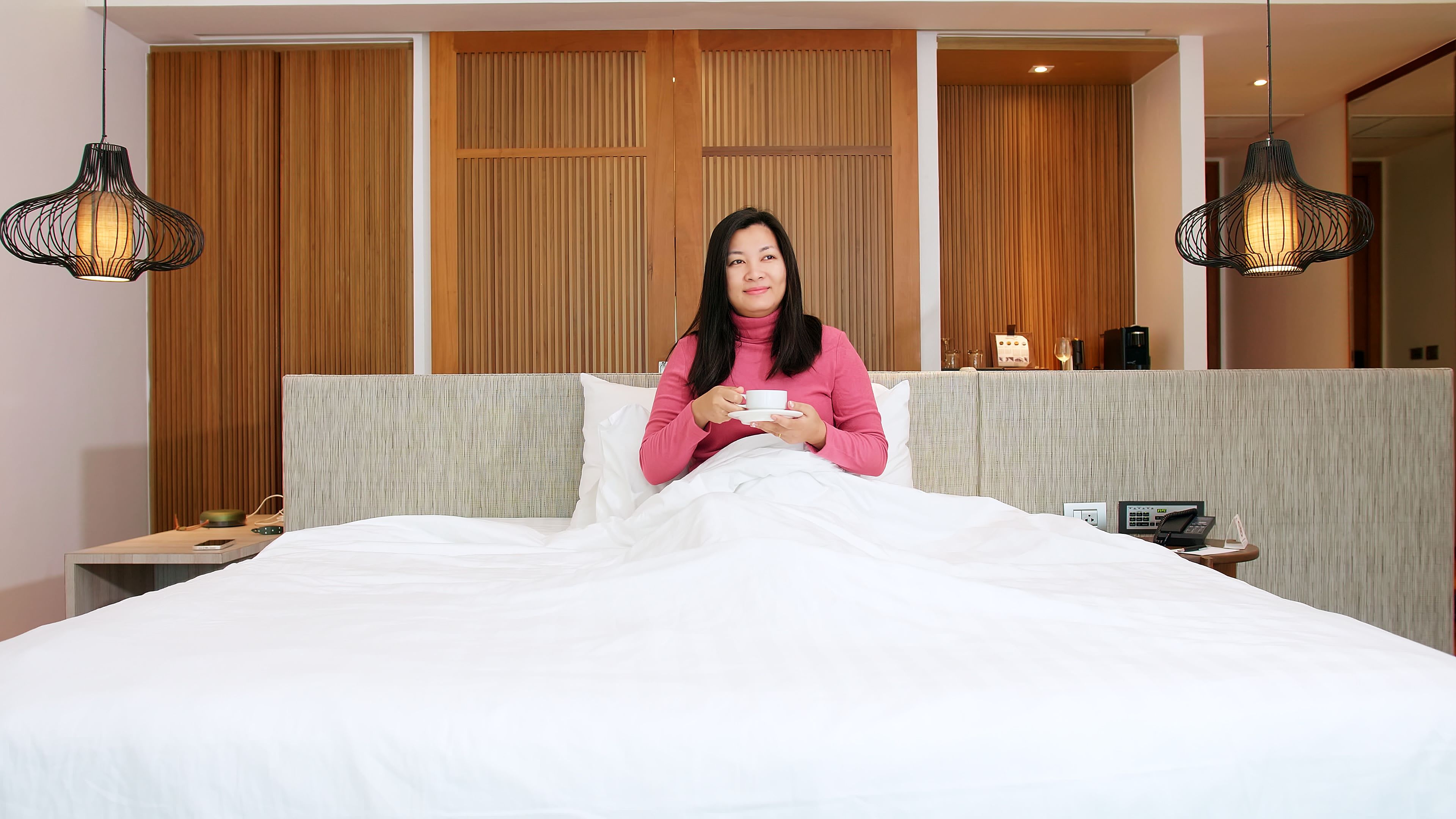 Phụ nữ châu Á đang nghỉ ngơi trên giường và uống cà phê vào buổi sáng