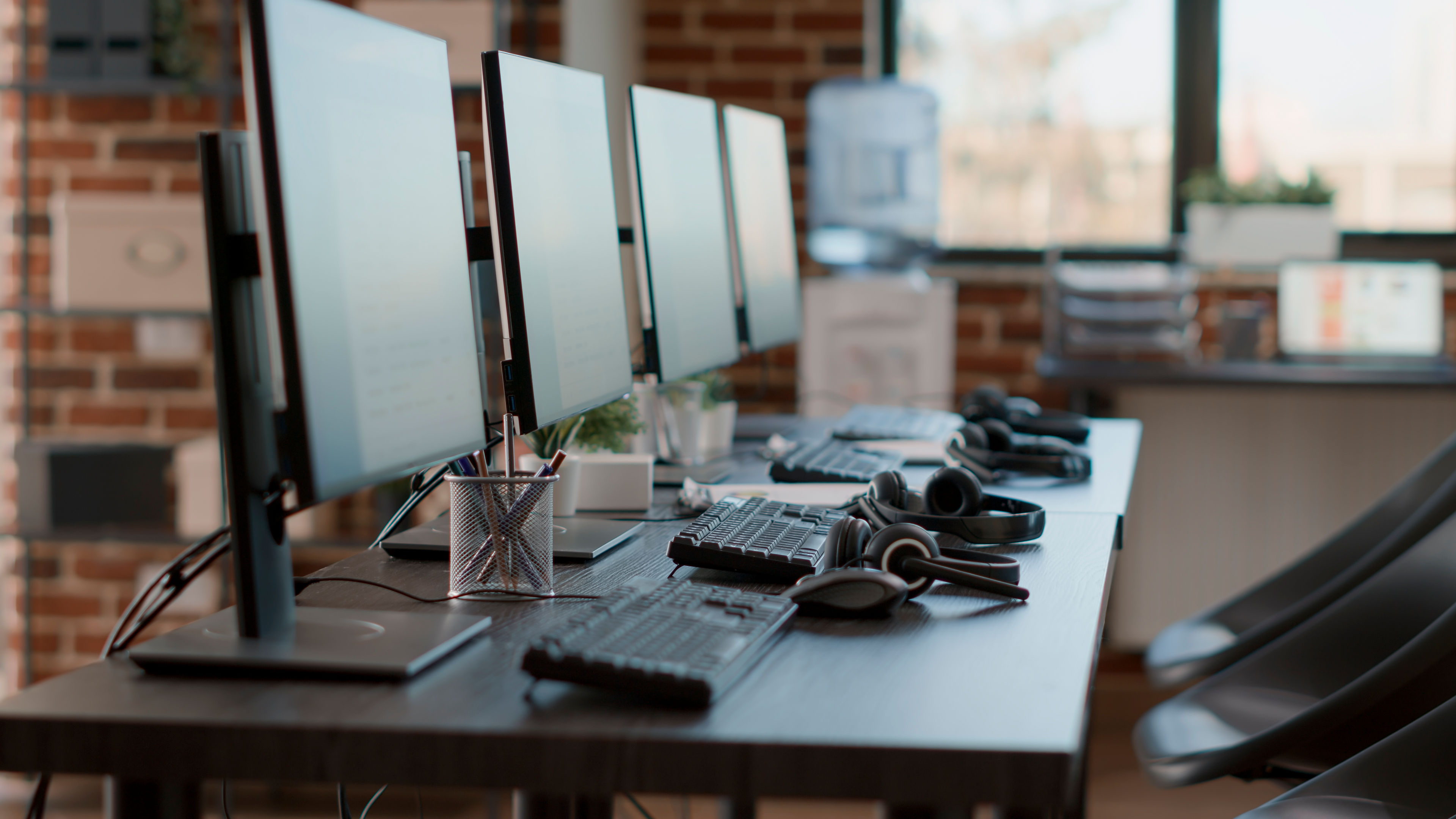 Empty workstation with monitors, keyboard, headset and office chairs in a clean office setting.