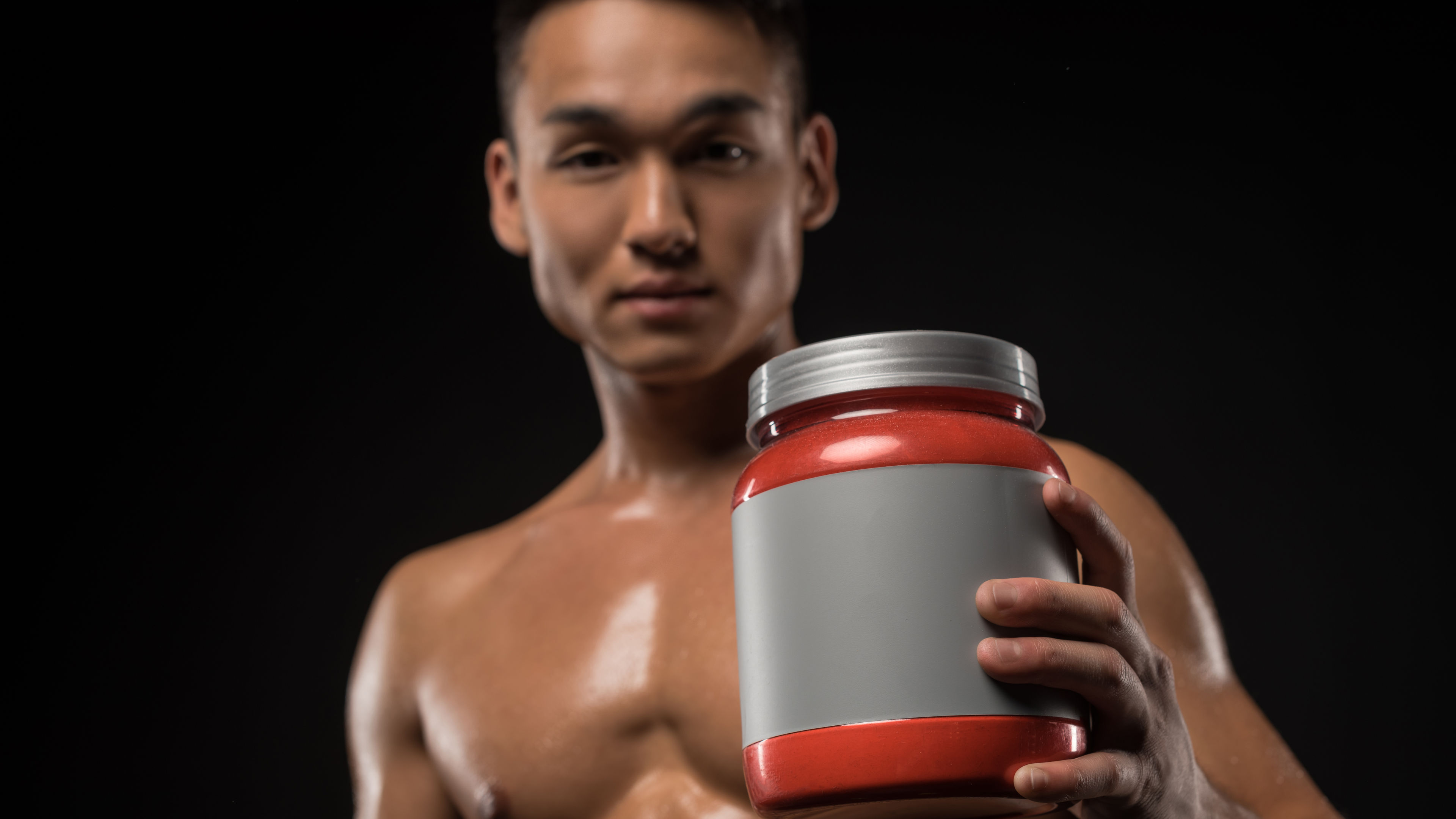 Close-up view of an Asian athlete holding a protein jar with a blank label.