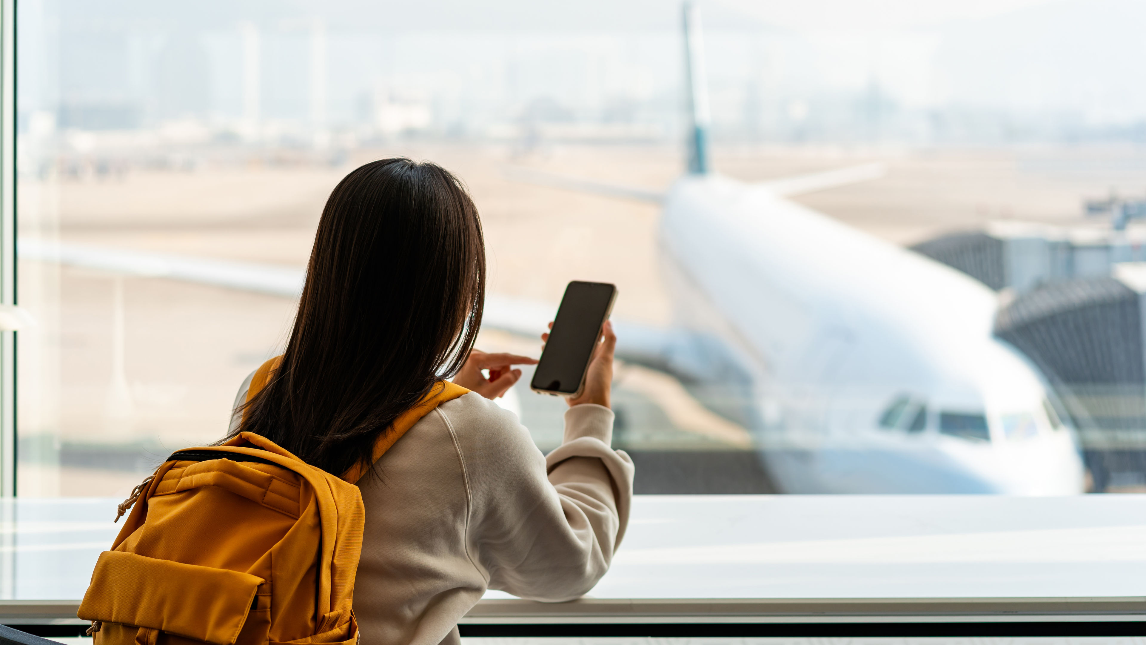 Young Asian woman traveler using smart phone while waiting for her flight at the airport.