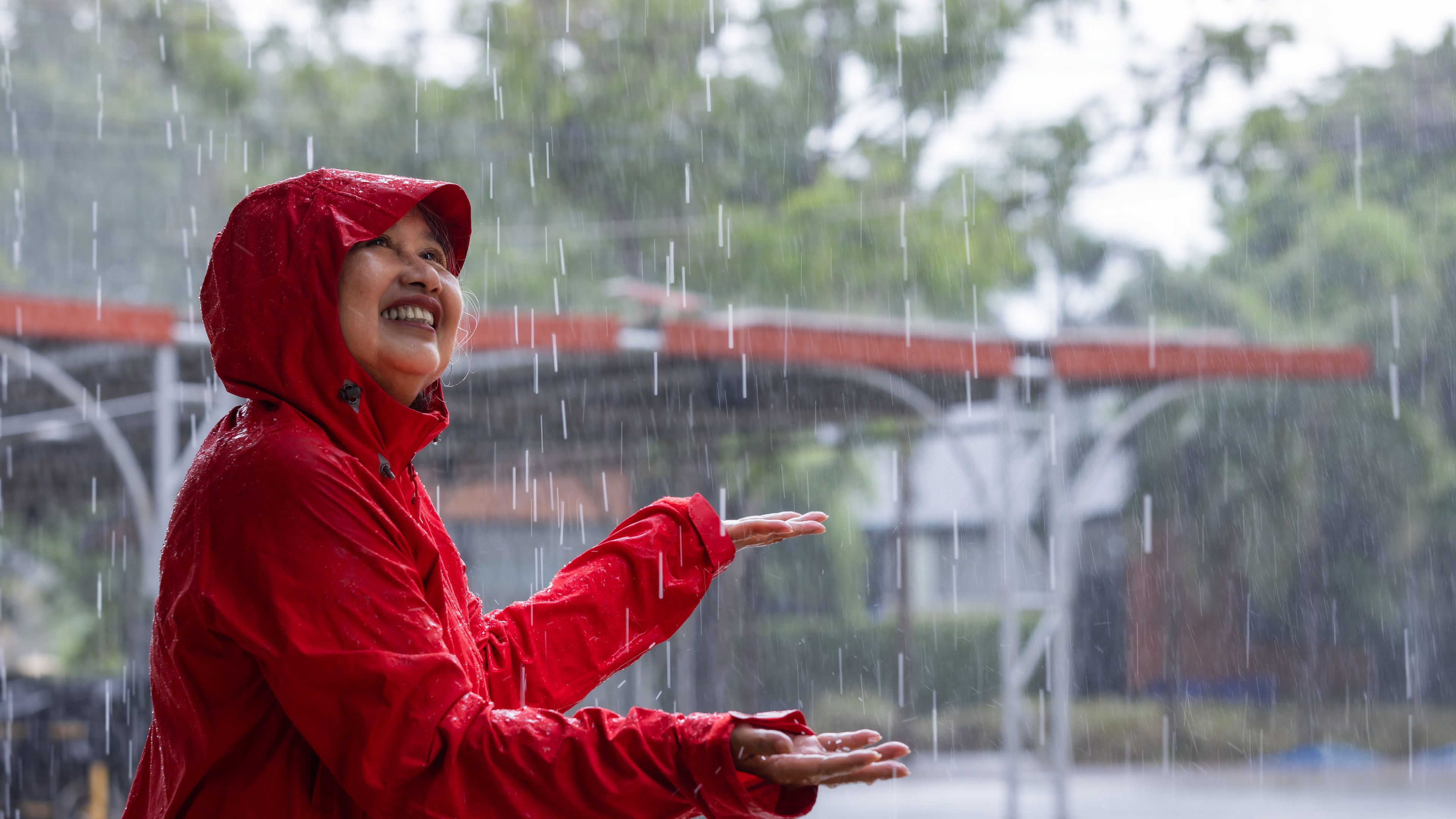 Joyful woman in red raincoat enjoying the rain with outstretched arm, surrounded by nature