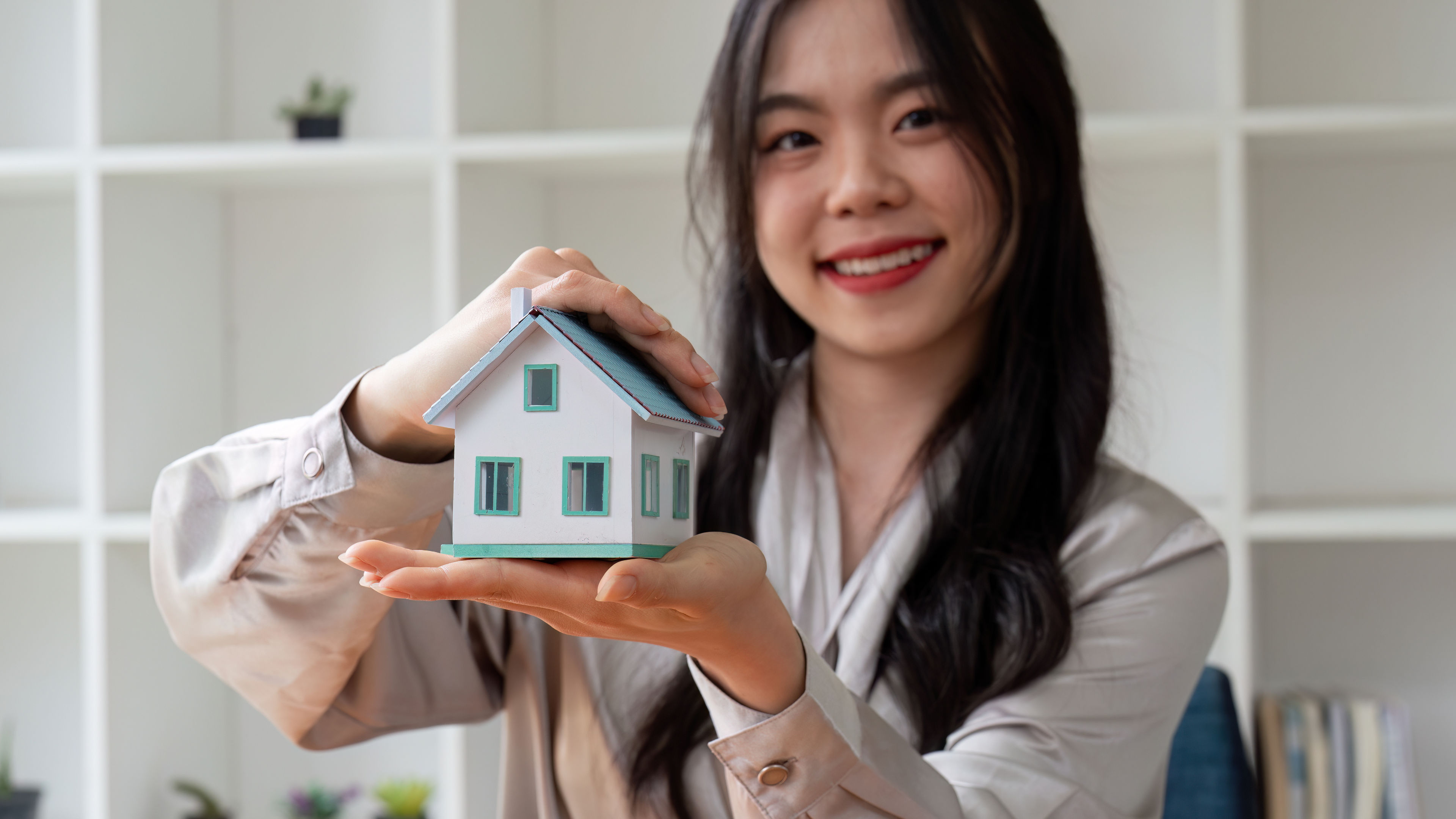 Smiling Asian woman holding miniature house model in hands.