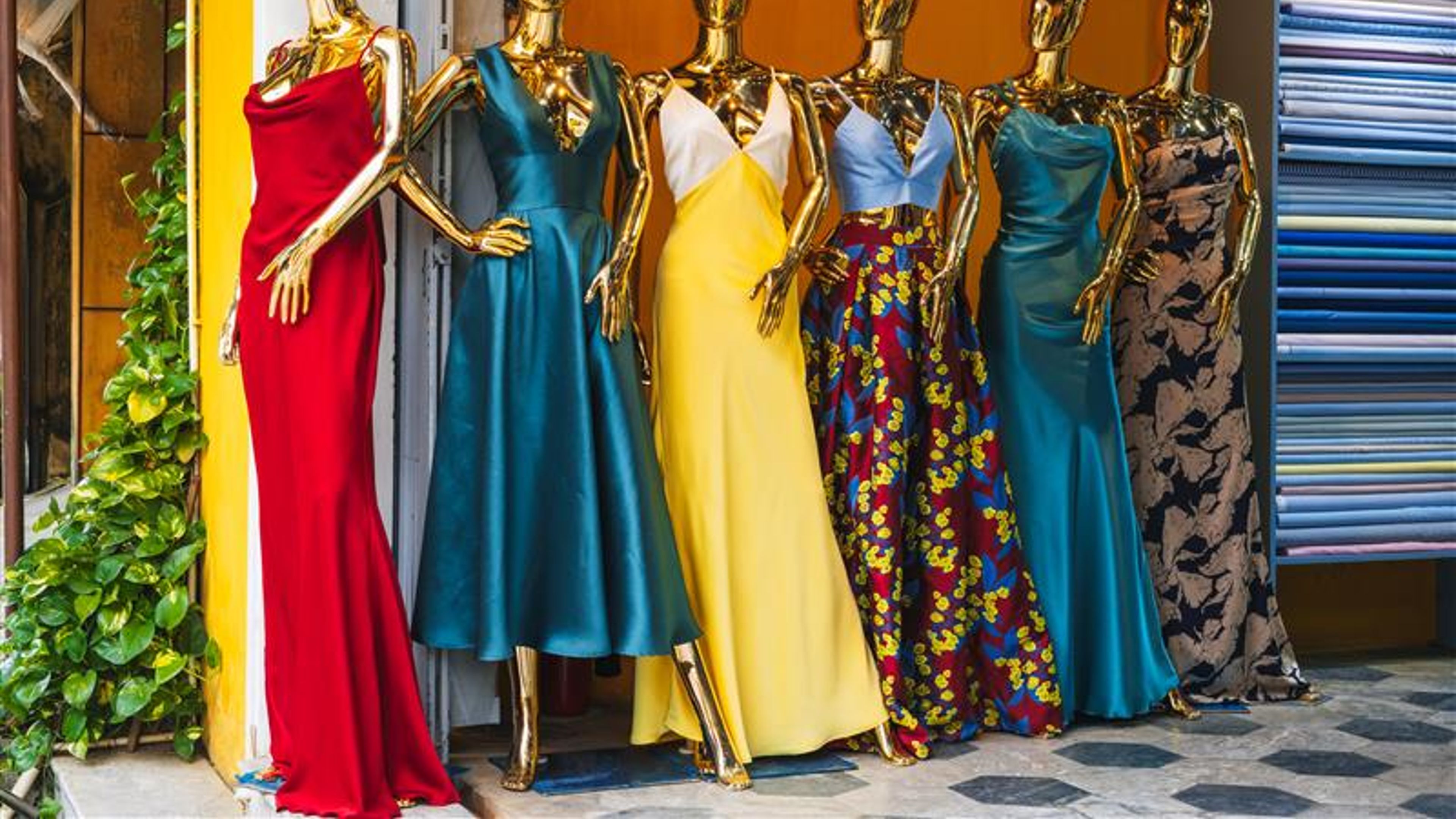 A group of mannequins in bright elegant dresses stands outside a women's clothing store 