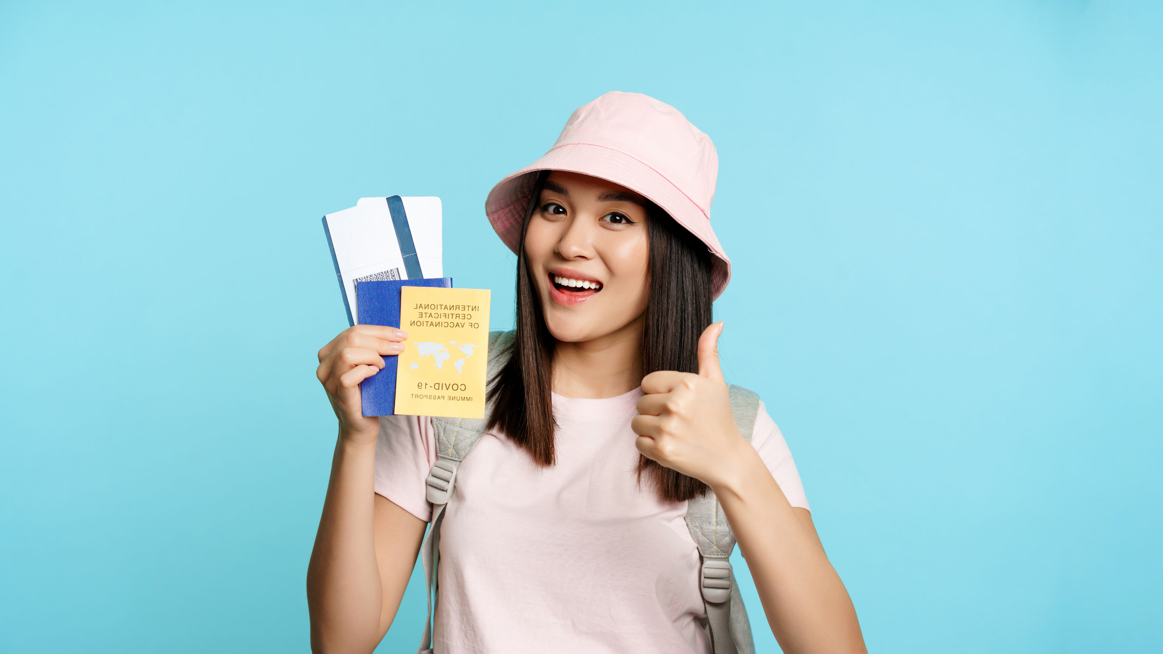 A happy traveler gives a thumbs-up while holding a passport, boarding pass 