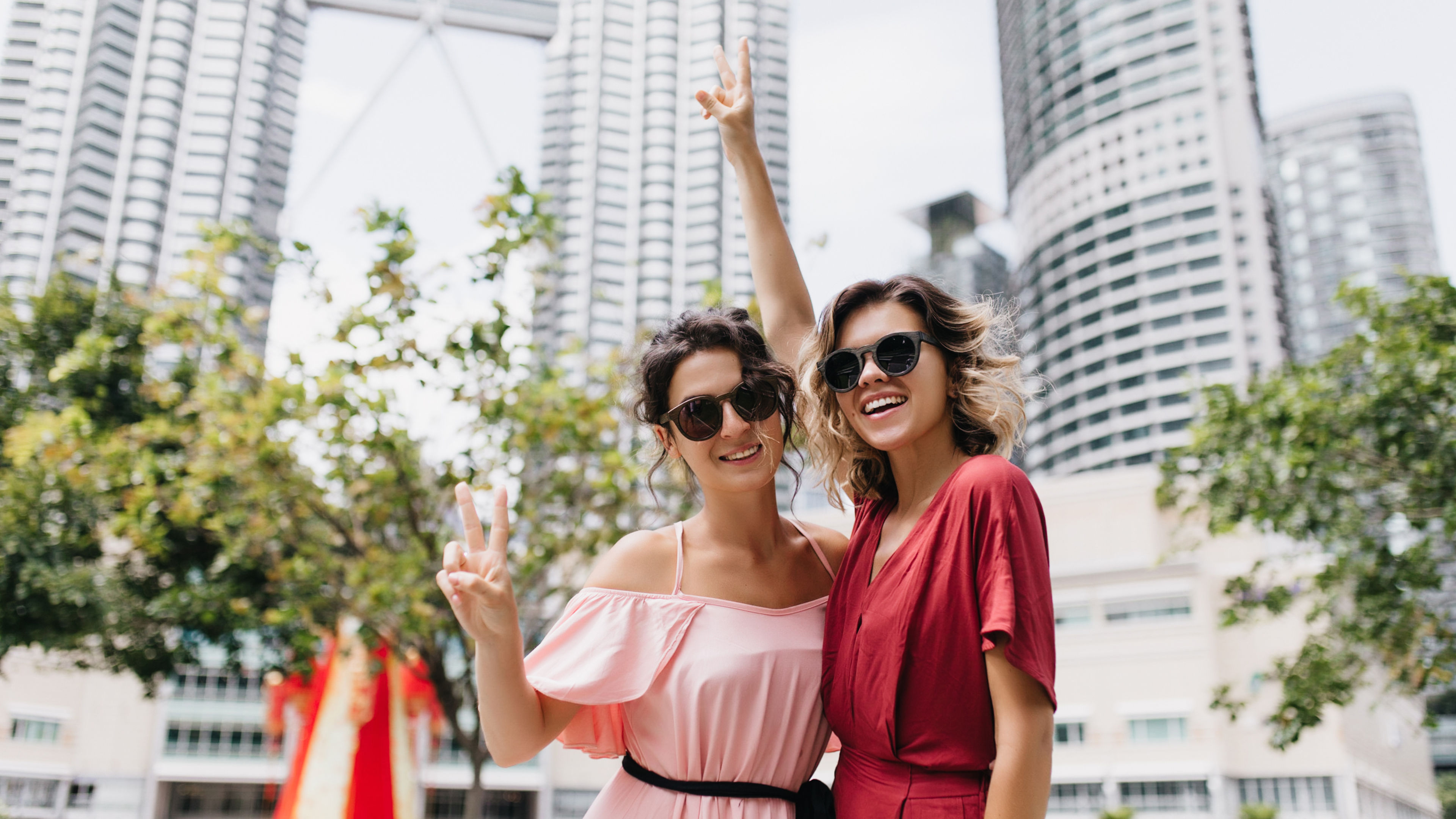 Blithesome girls in modern attire posing with skyscrapers on background. Outdoor shot of carefree  