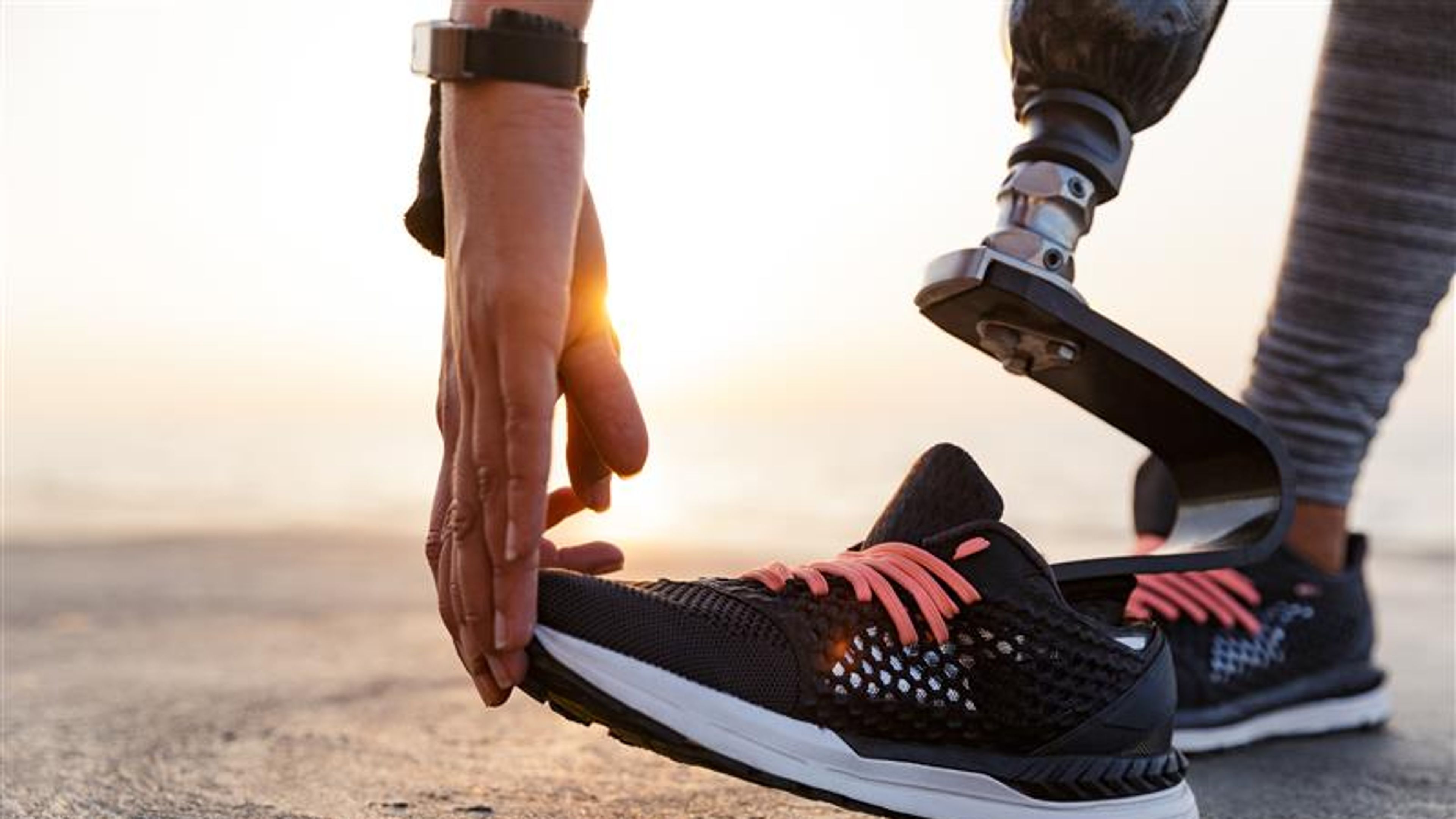 Close up of motivated disabled athlete woman with prosthetic leg doing stretching exercises outdoor at the beach 