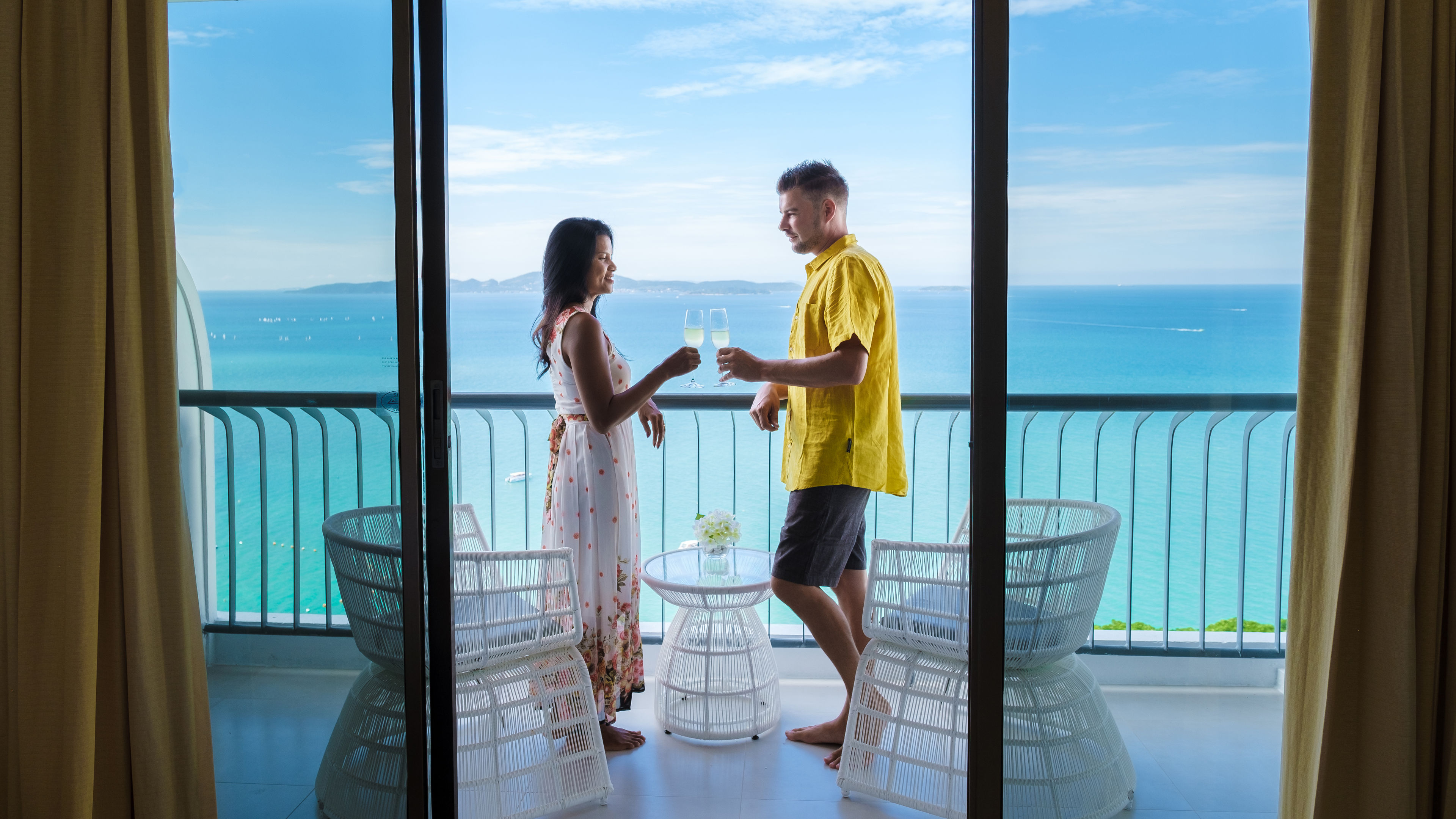 Couple toasting with champagne on a balcony overlooking the ocean.