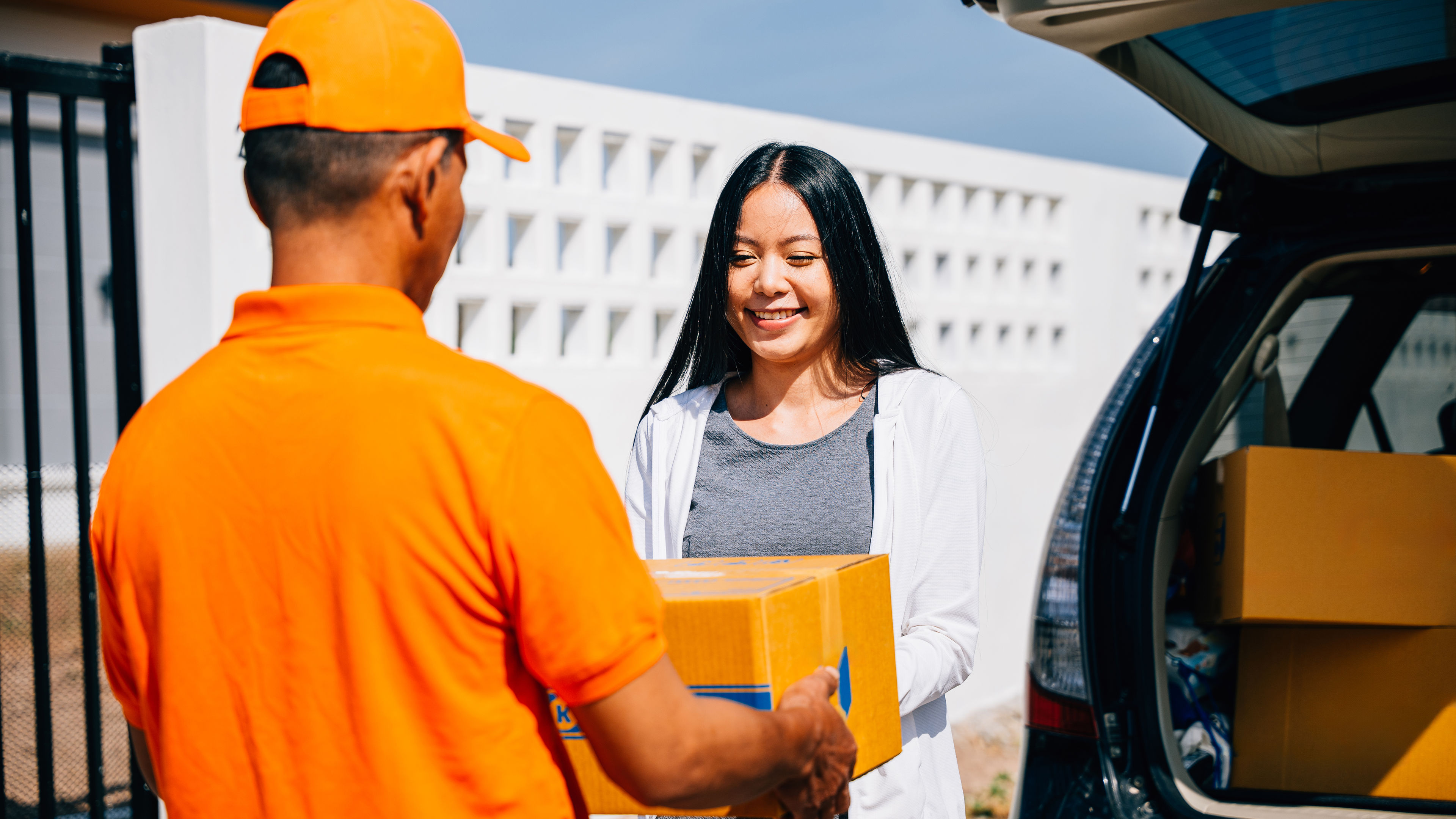 Efficient delivery logistics illustrated with a courier handing a cardboard parcel to a smiling woman customer at her home.  