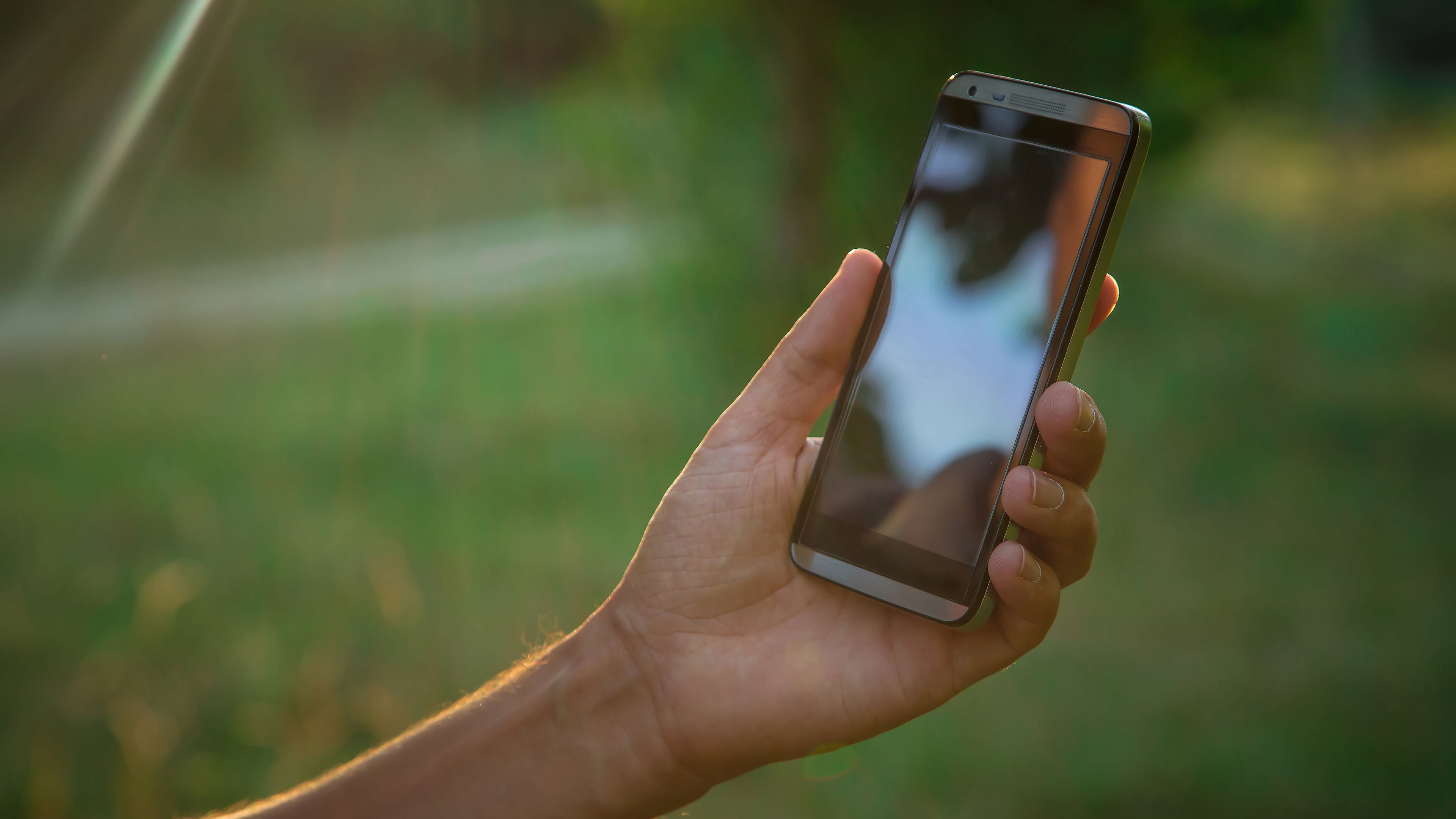 hand hold black smart phone, cell phone, mobile over blurred image of green forest background 