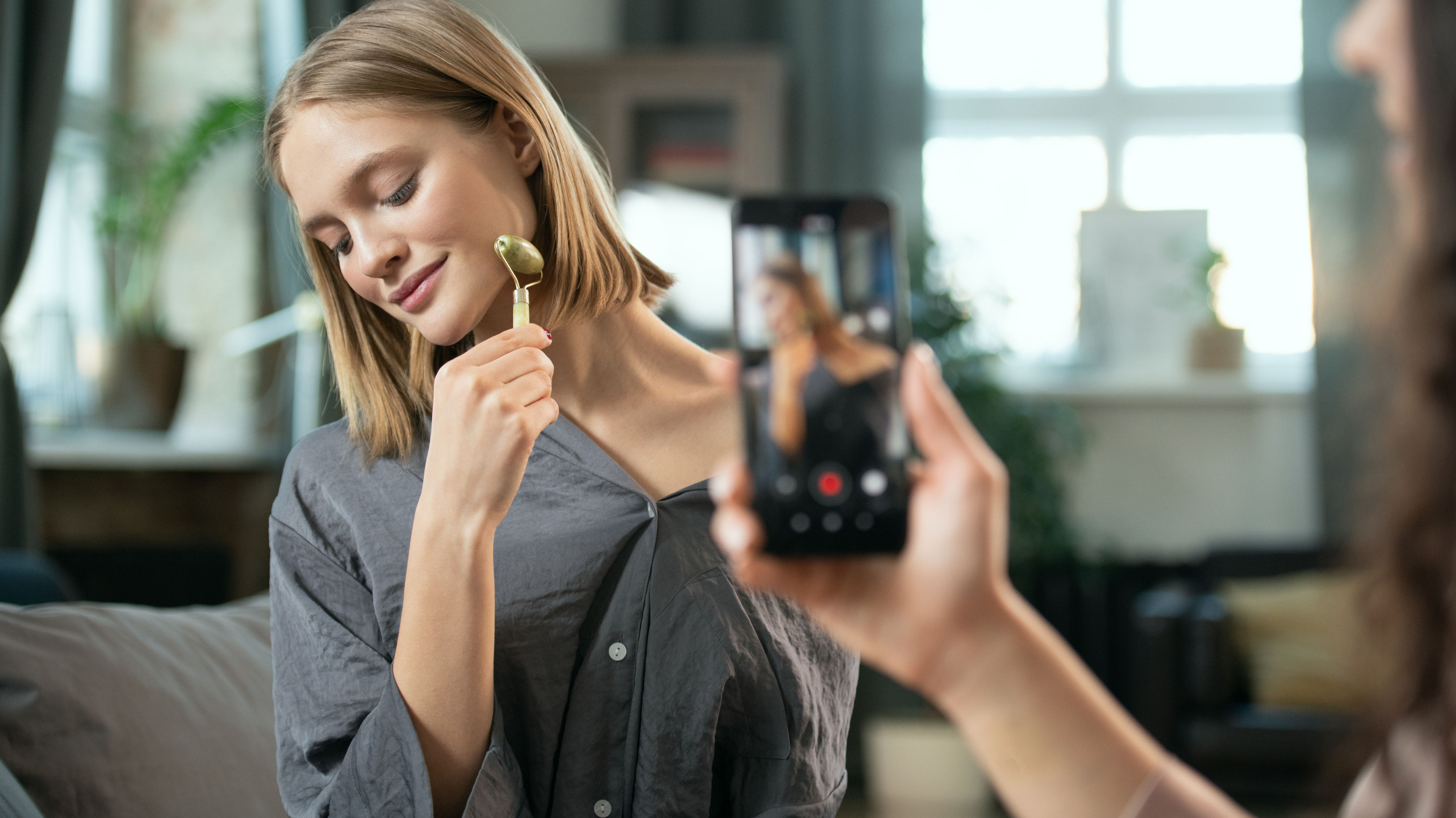 Hand of young woman with smartphone shooting her friend using massage roller 