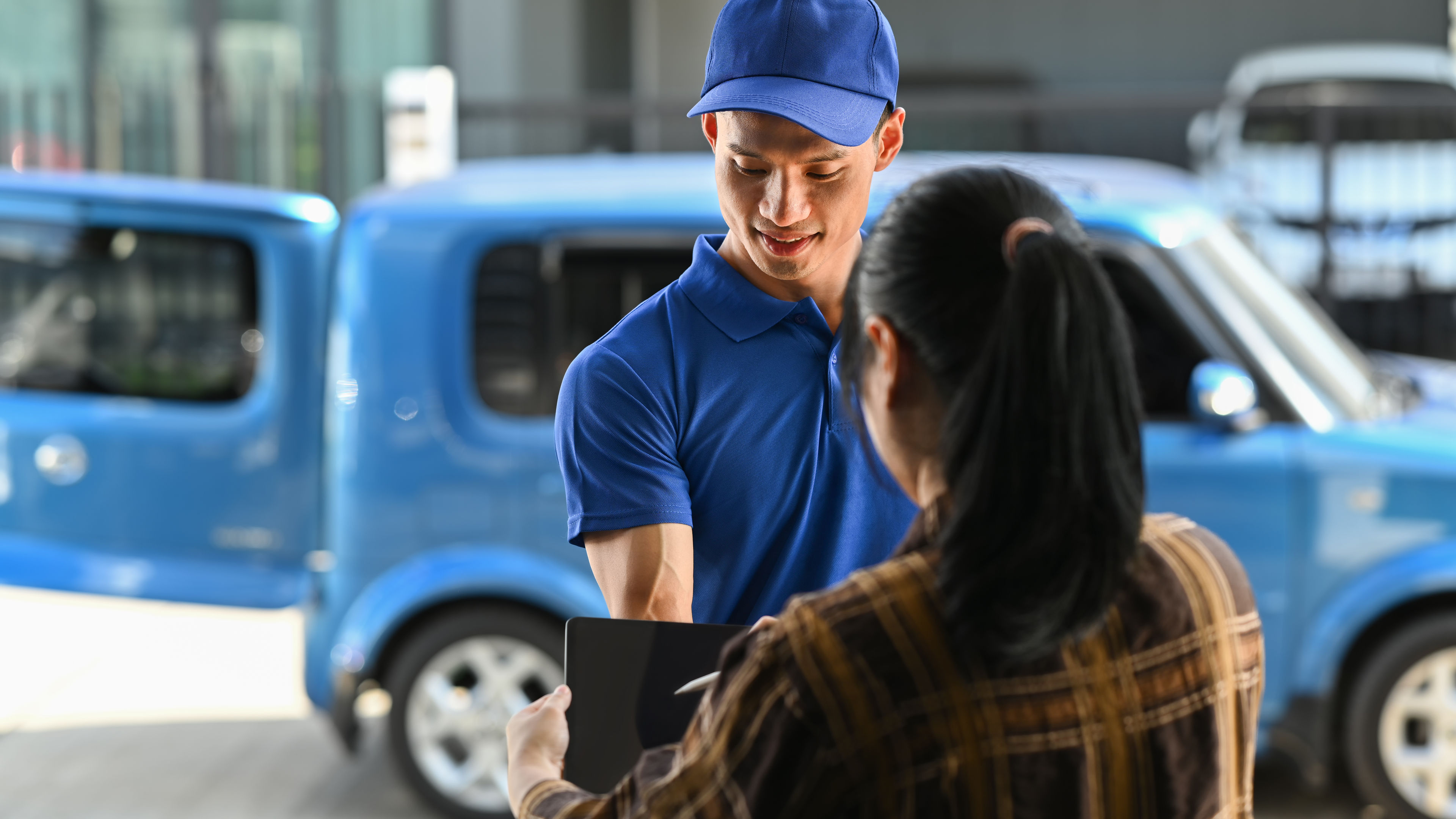 Rear view of female customers signing on digital tablets and receiving courier parcels. Delivery service concept. 