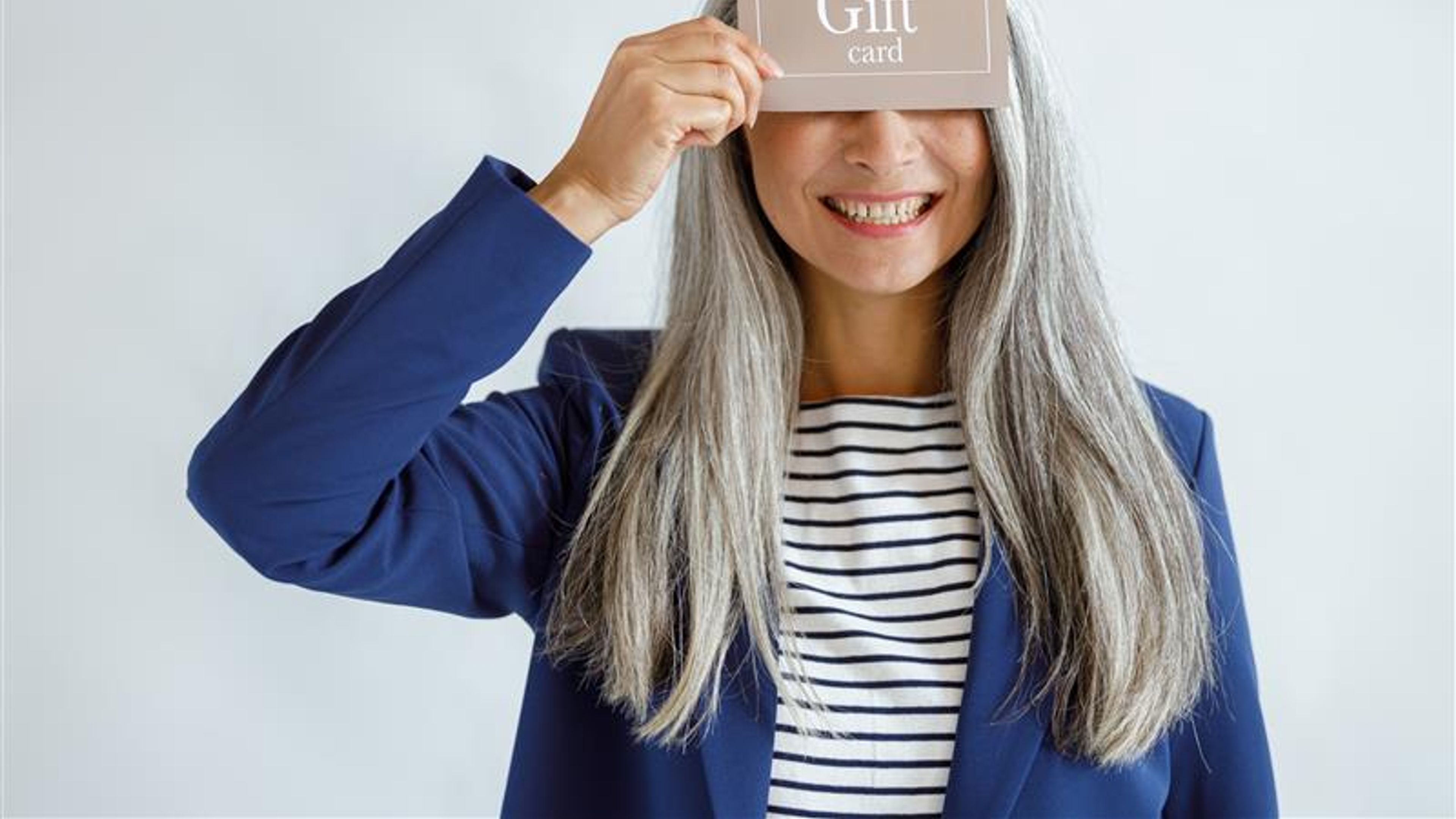 Smiling mature lady with loose silver hair in blue jacket holds gift card 