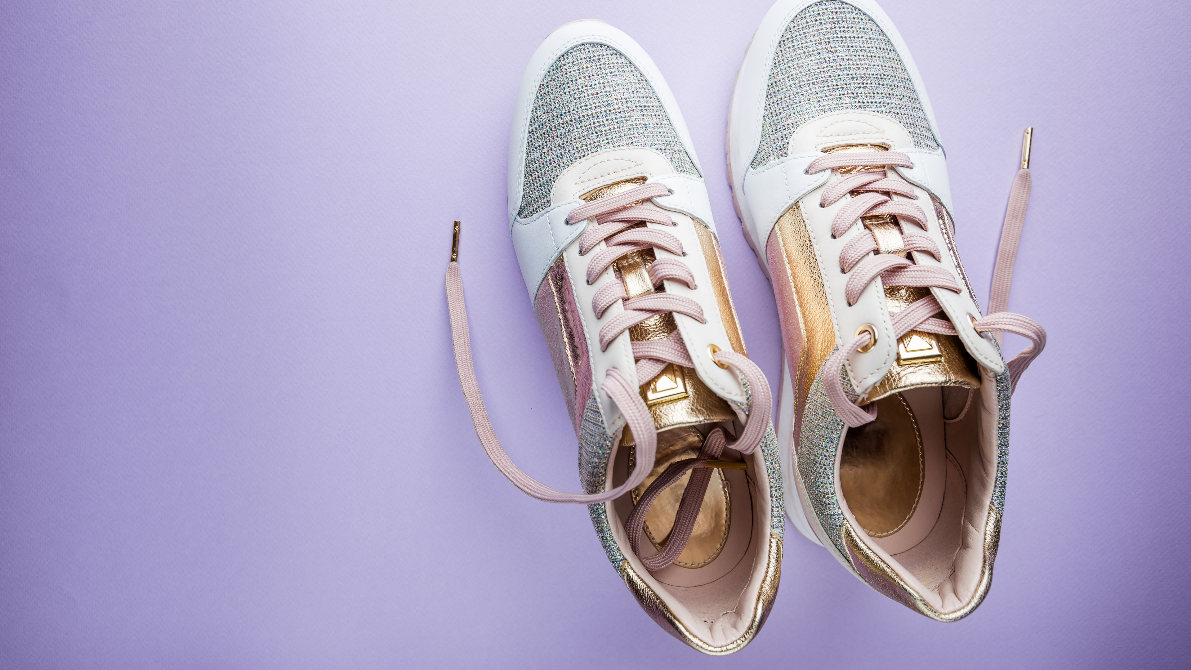 Stylish sneakers with metallic and pastel accents placed on a soft lavender background, with loosely tied laces adding a casual touch. 