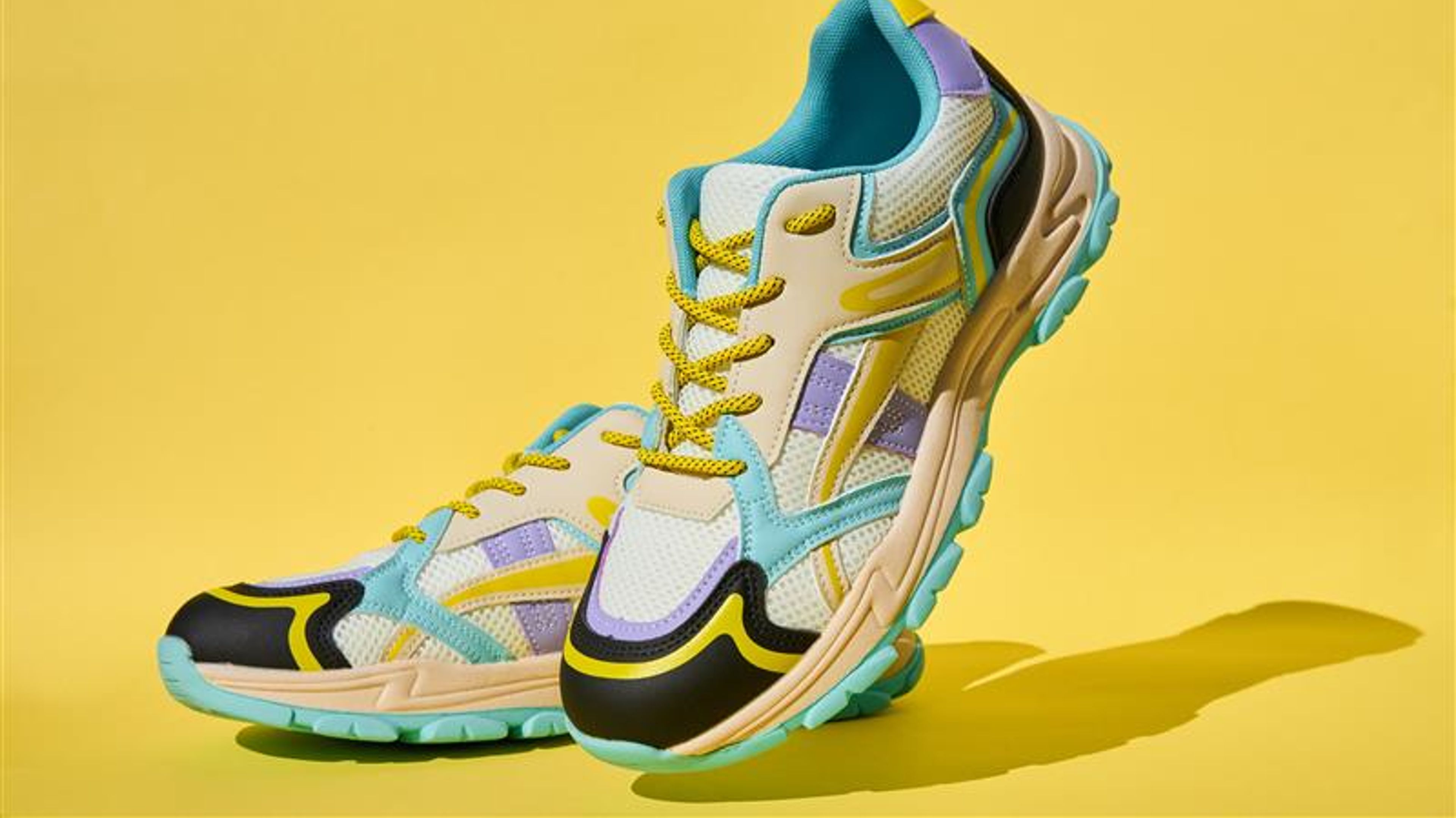 White sneakers with colored accents on yellow background, Pair of fashionable sport shoes 