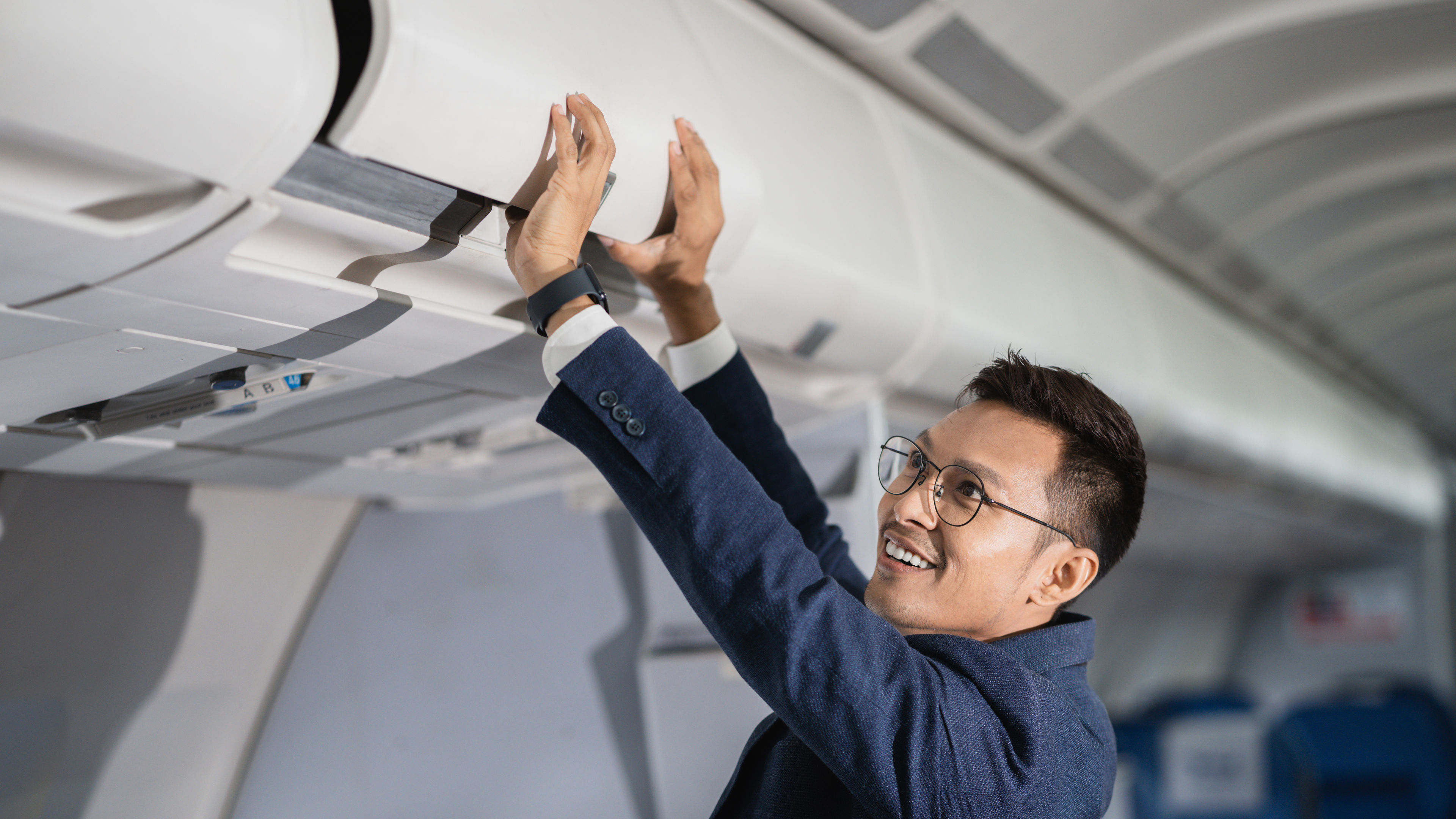 A young Asian man in blue loading luggage in the flight cabin.