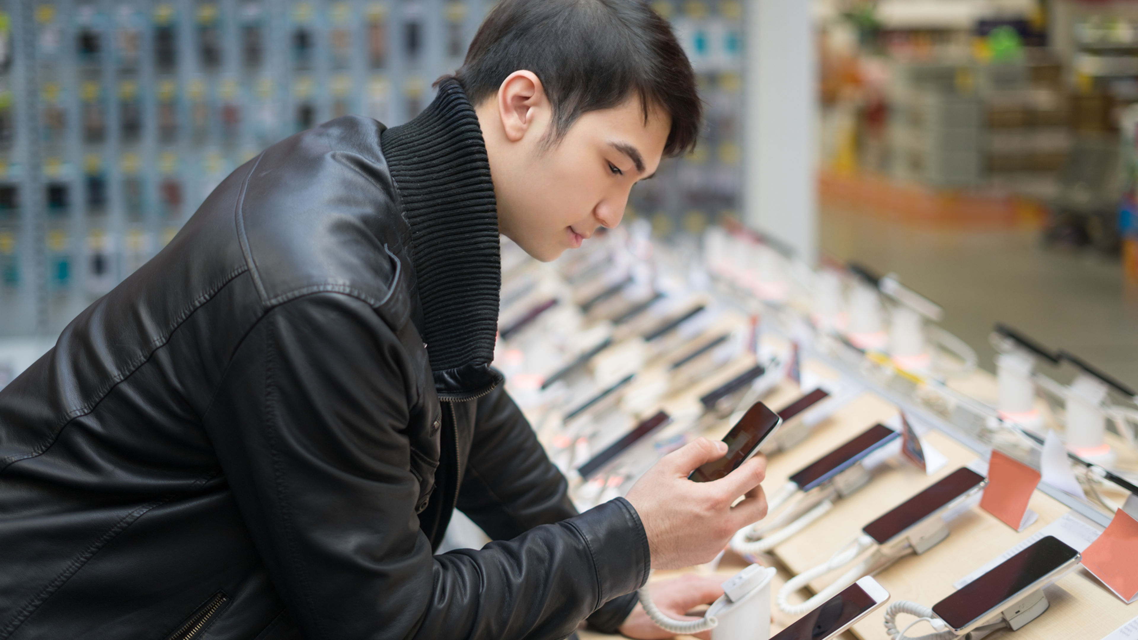 An Asian man in black jacket checking mobile phones in a shop.