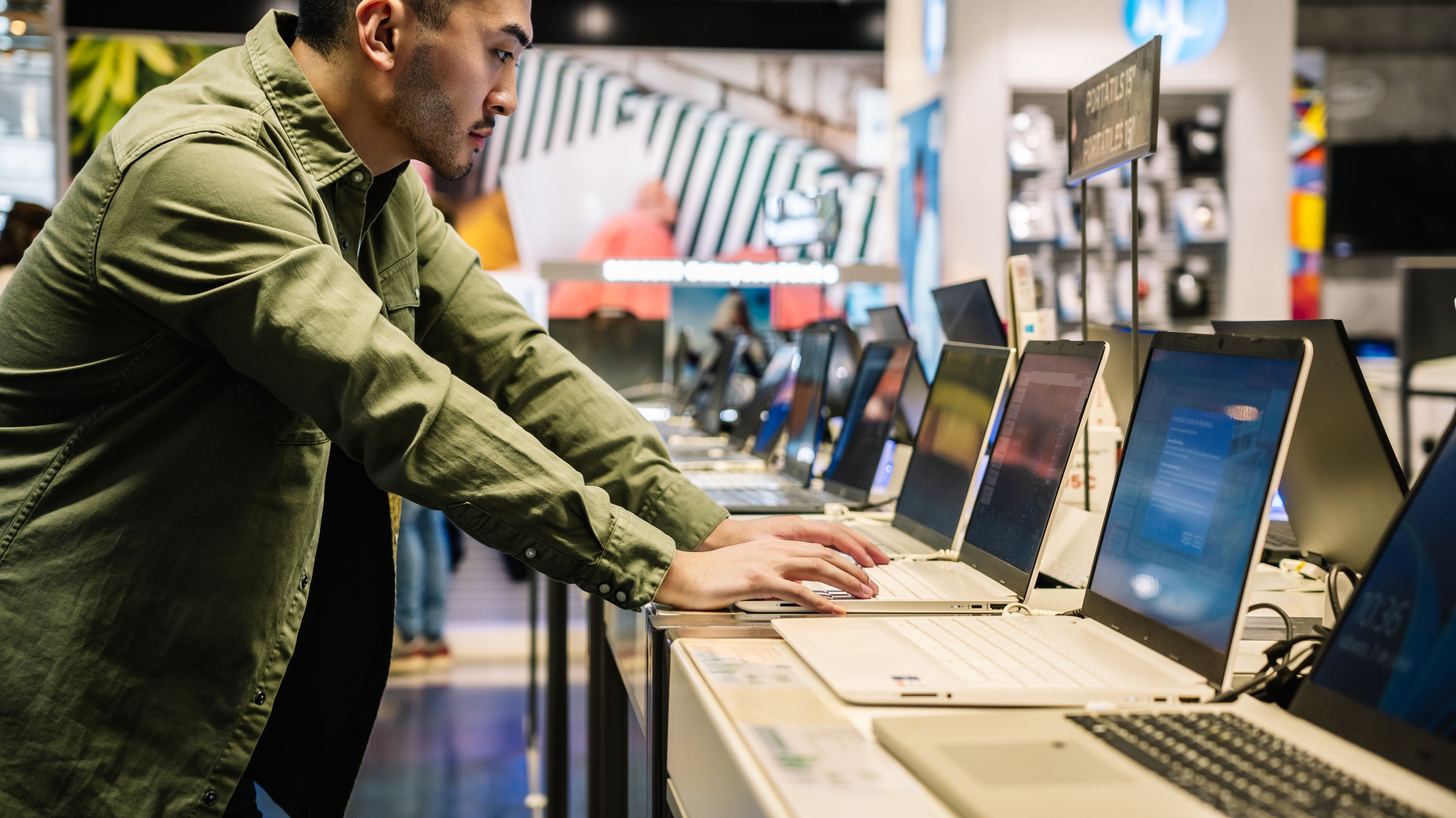 Focused ethnic man choosing laptop in shop