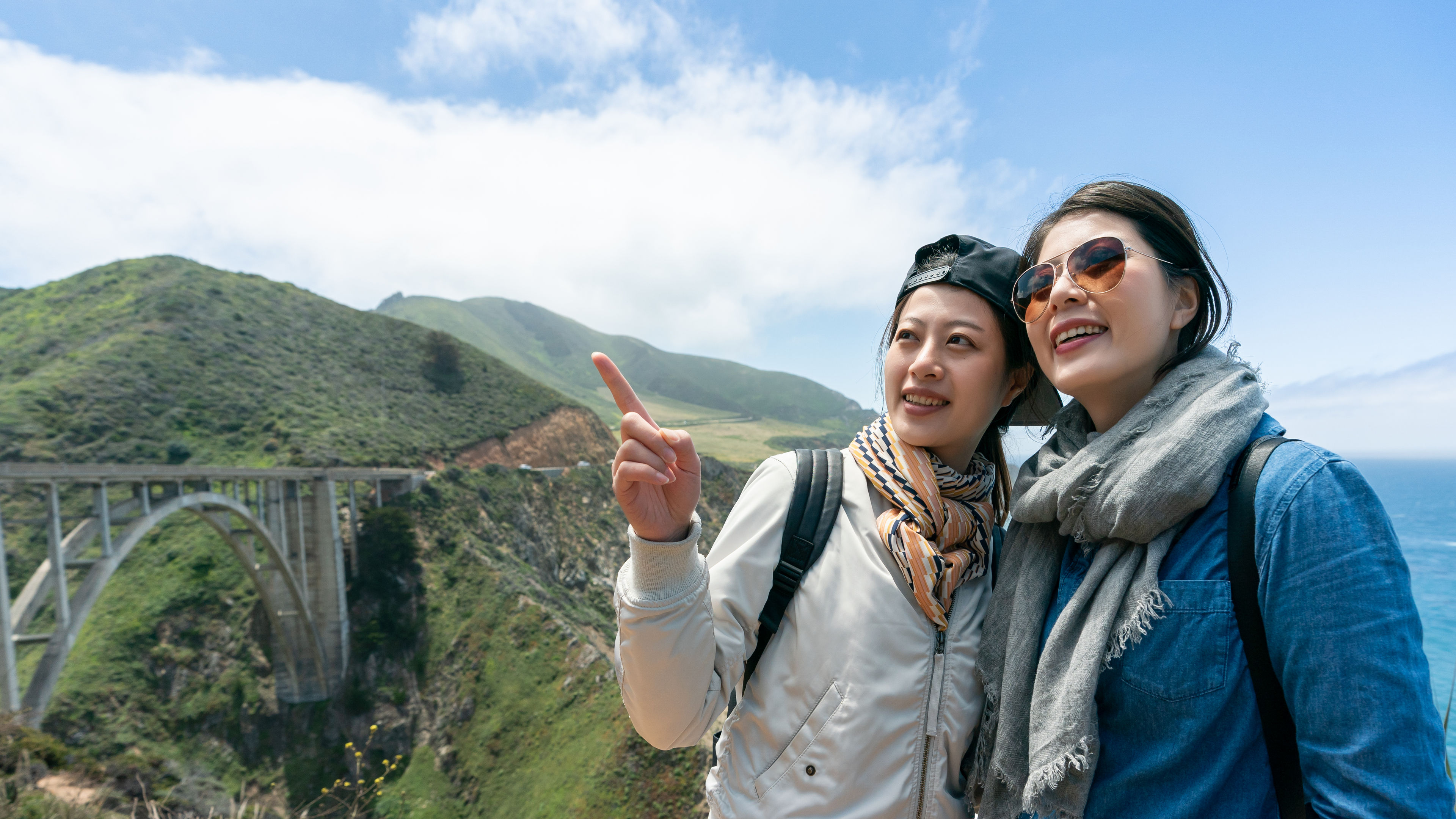 Friends enjoying coastal views near a historic bridge, smiling and taking in the moment.