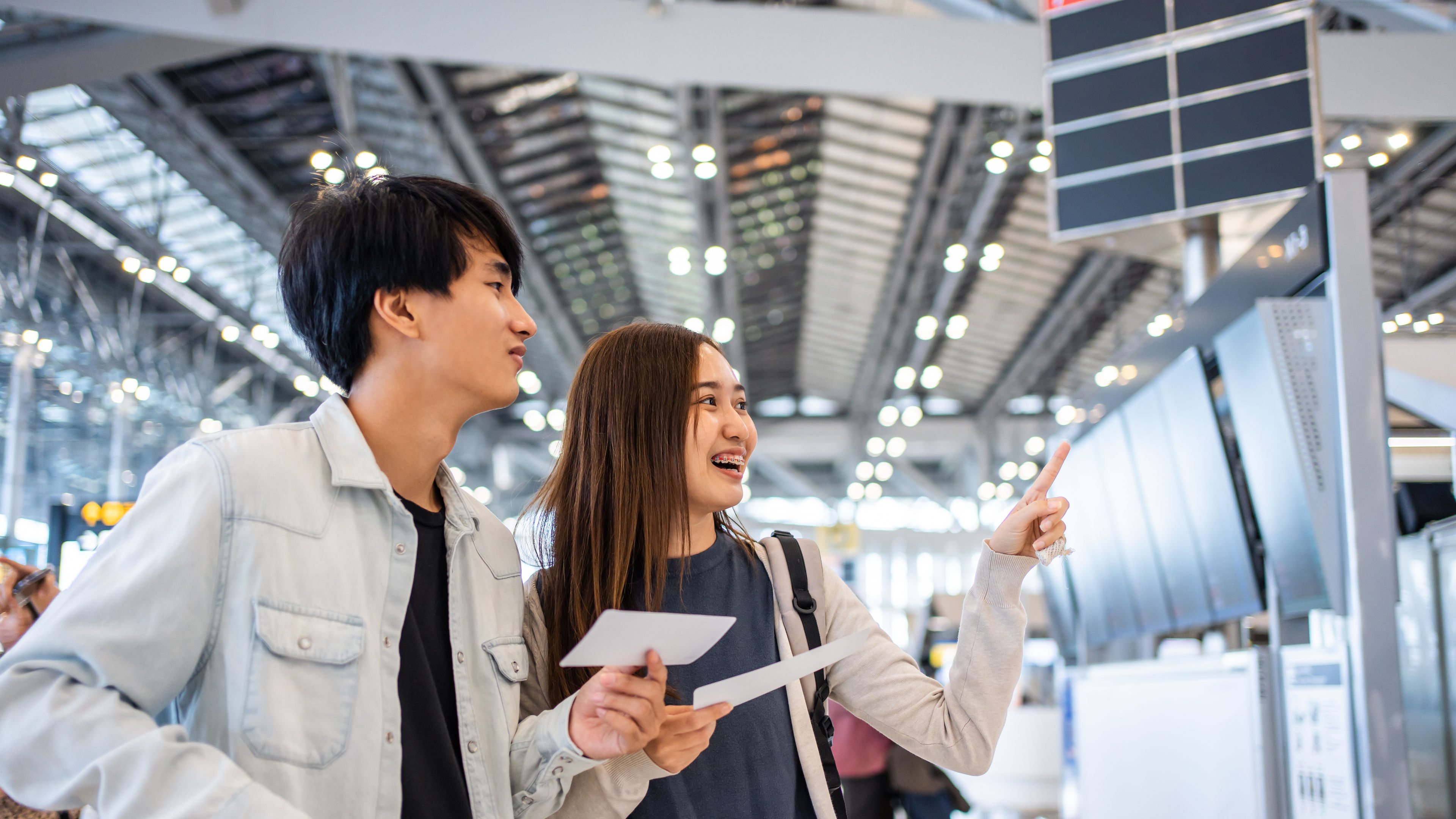 Two friends in an airport with tickets in hand