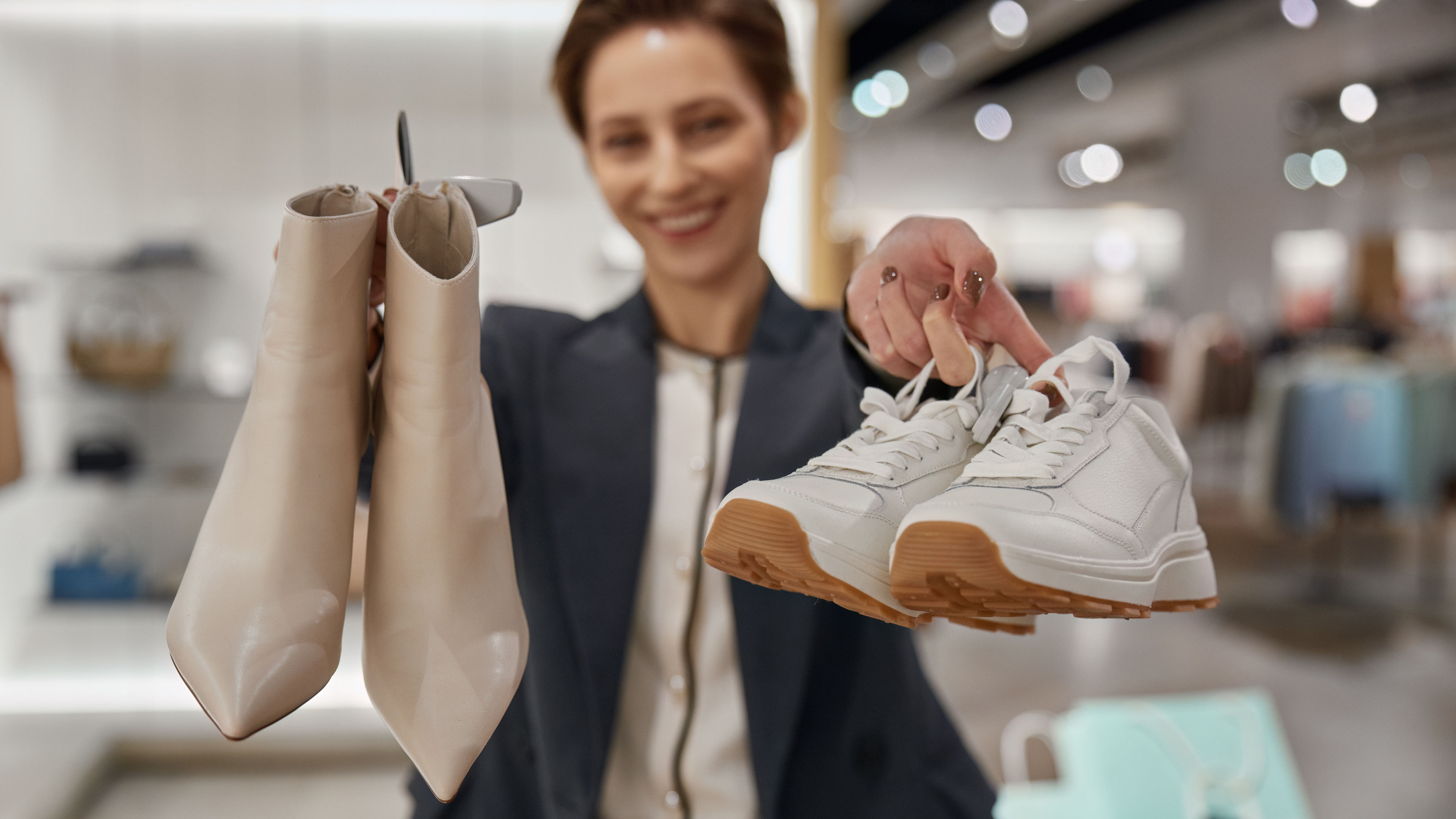 A woman standing by holding a pair of fashionable boots and sneakers.