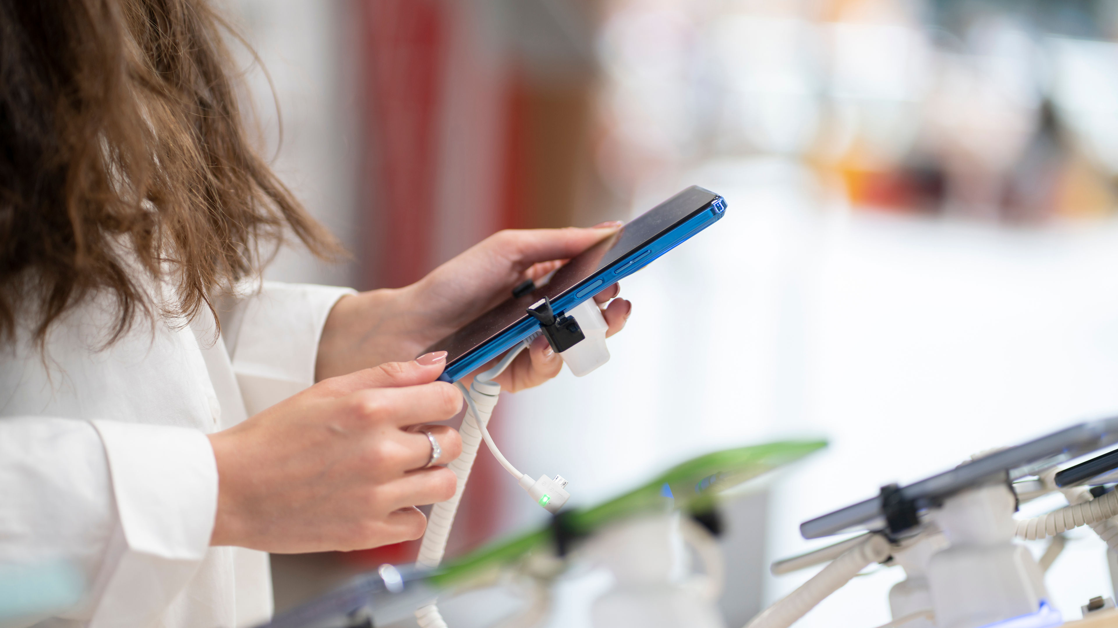  a woman in an electronics store holding a charging cable to use in her phone.