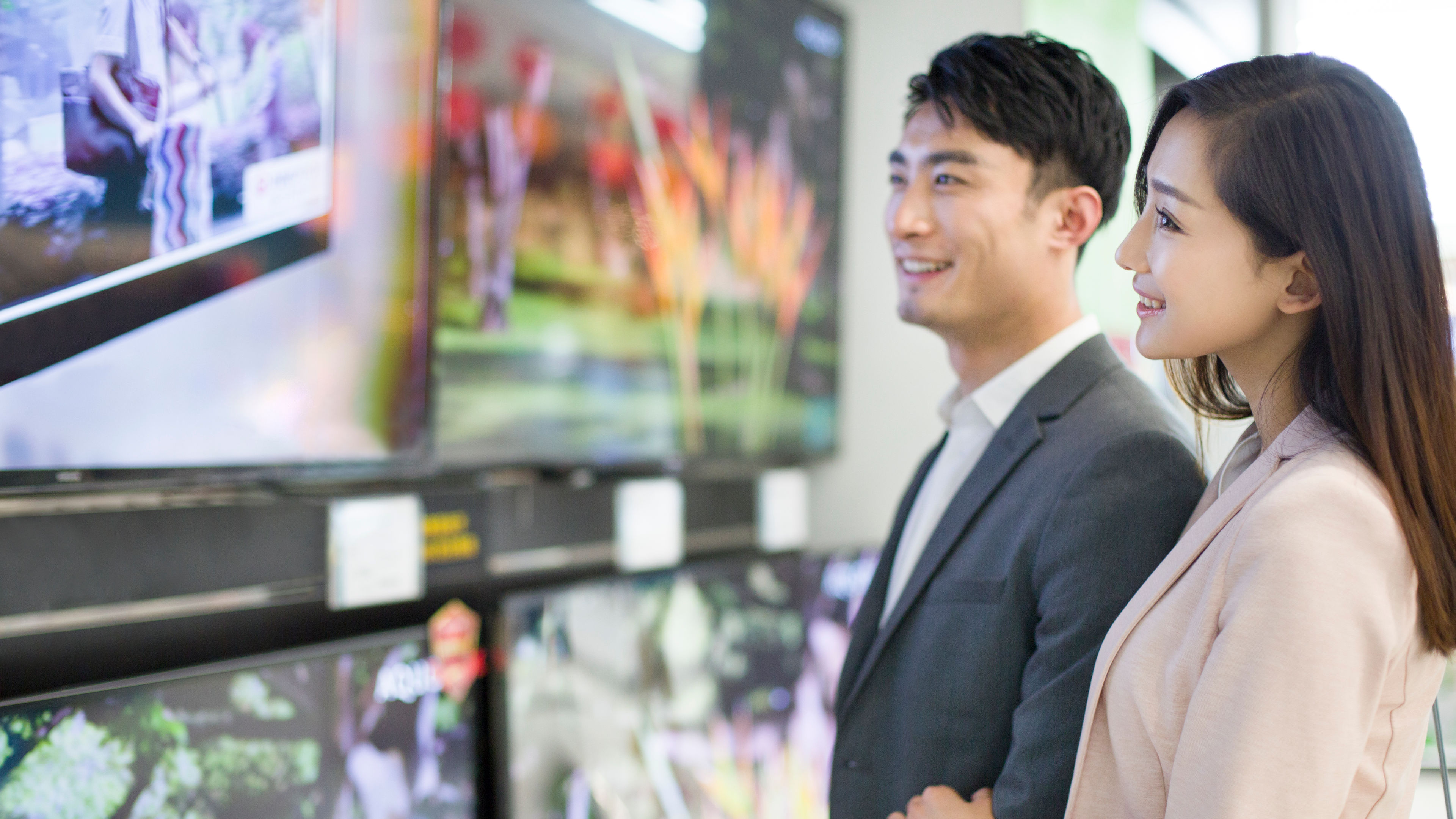 A young Asian couple examining a television in an electronics store.