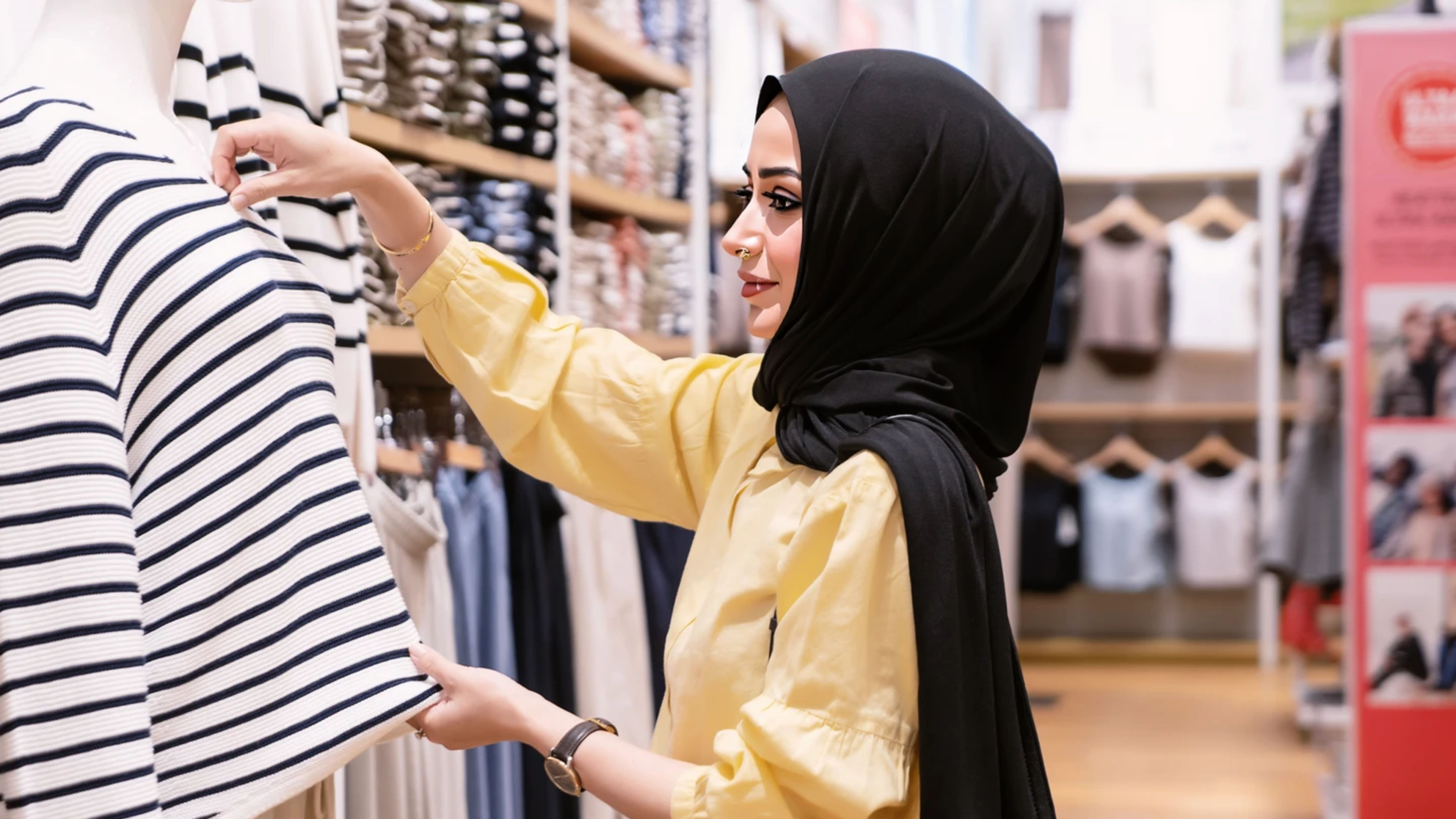 Woman wearing a hijab browsing a striped shirt in a clothing store.