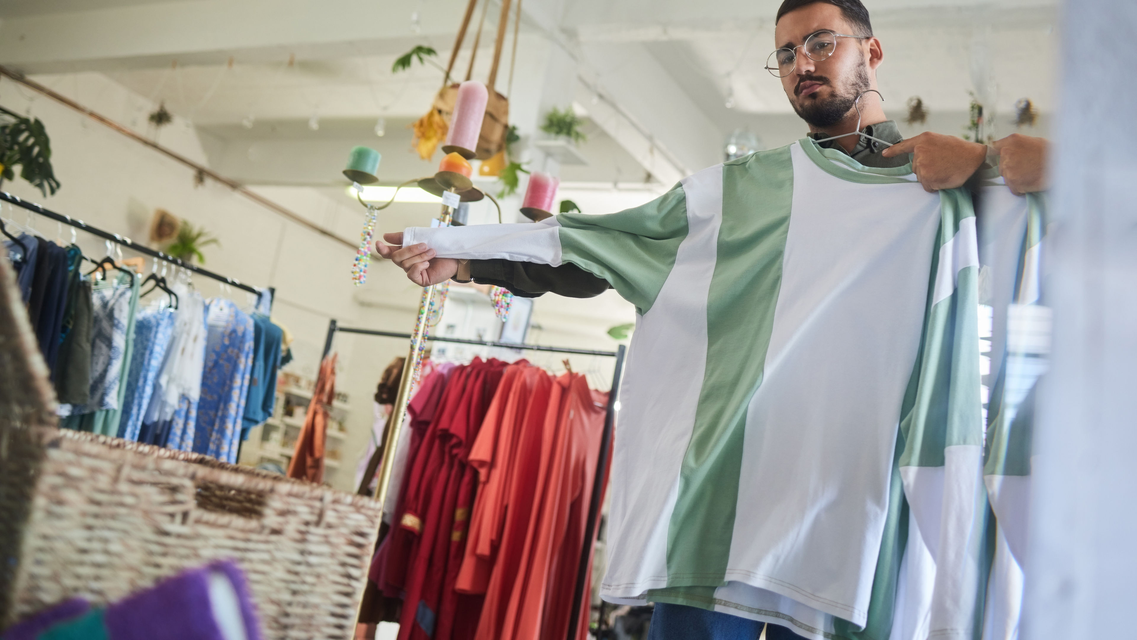 A man standing inside the shop, casually holding a T shirt in his hands.