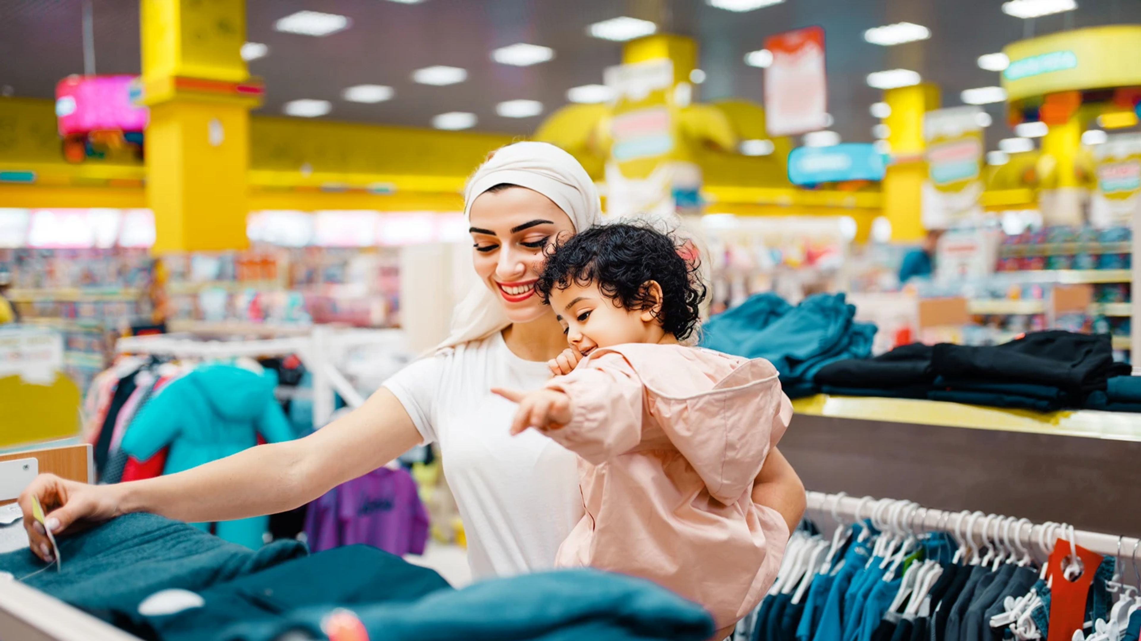 Arab mom and baby in light coloured dress browsing clothes on a mall.