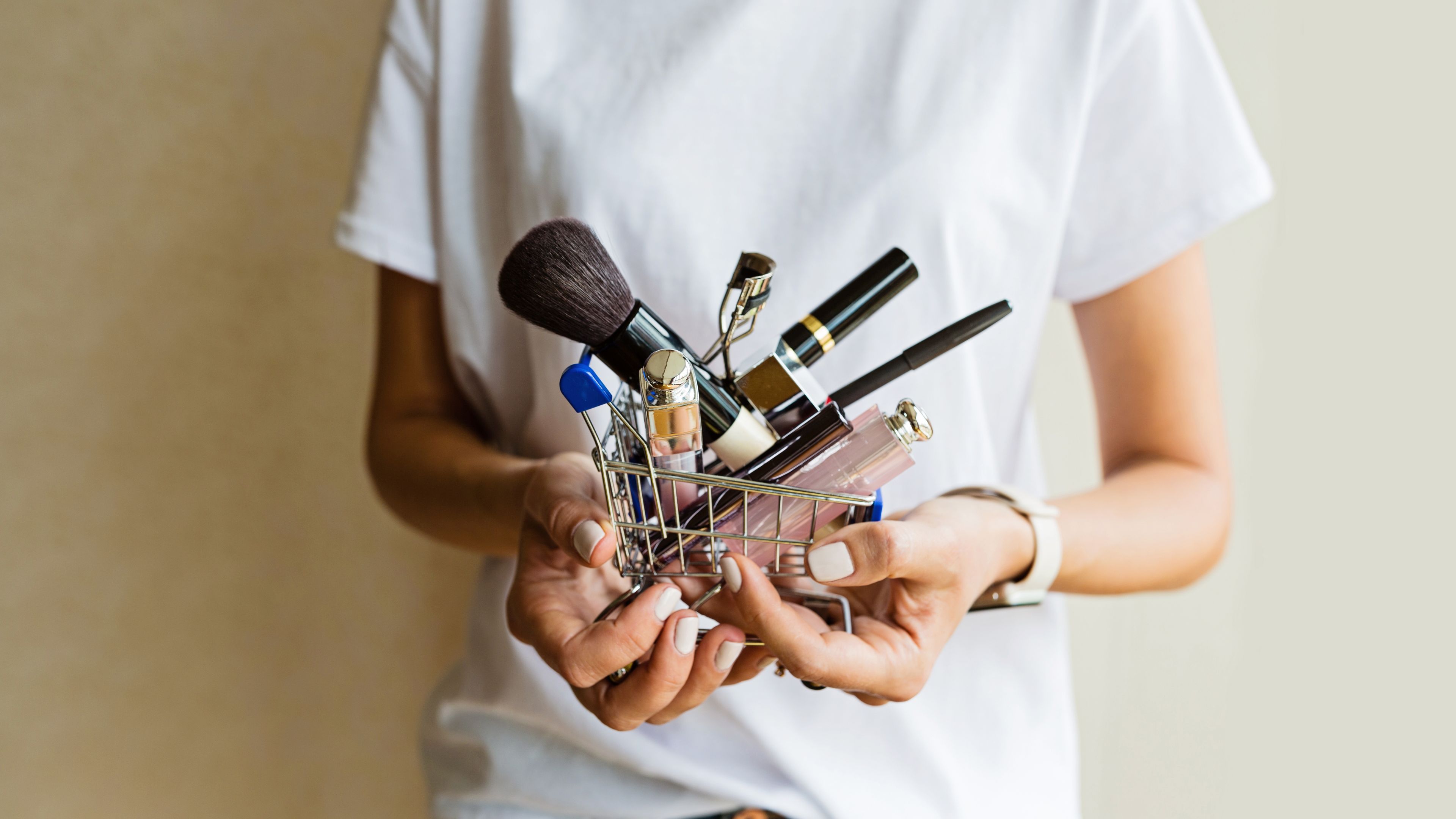 A small shopping cart filled with makeup items held in a hand.