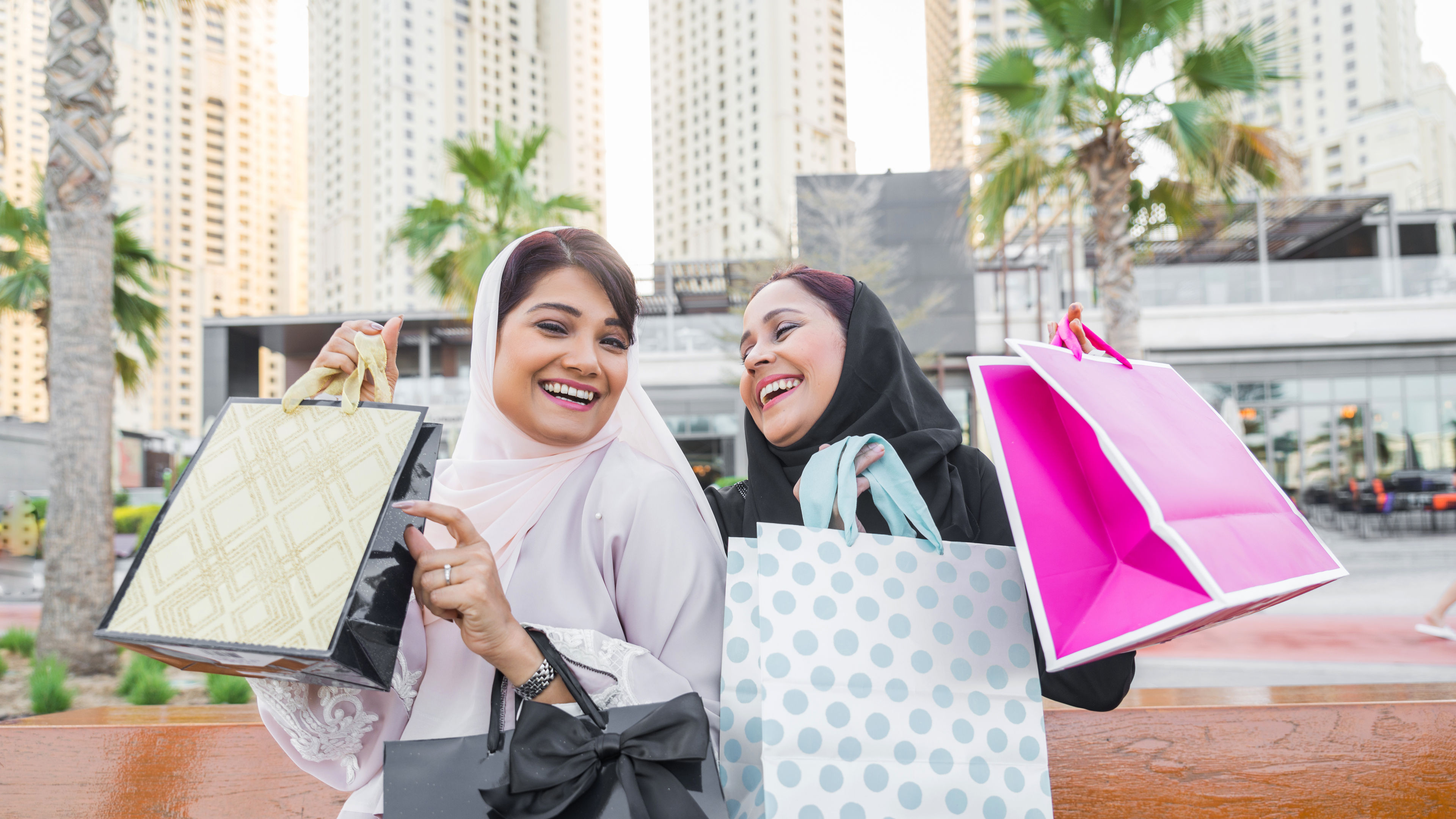 Two women shopping outdoors together, having fun with shopping bags in their hands.