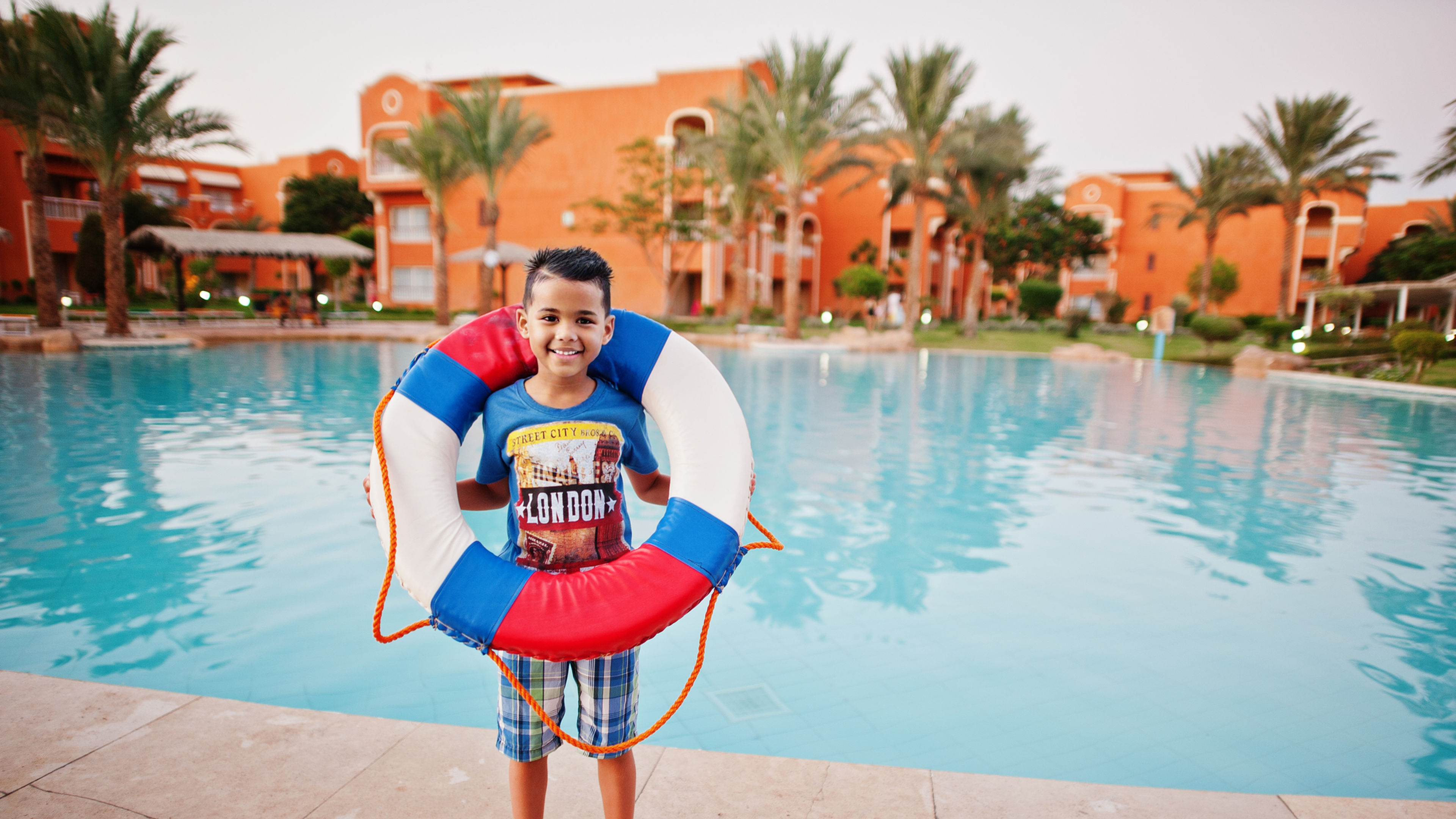 Boy with lifebuoy standing by a pool at a resort posing for the picture.