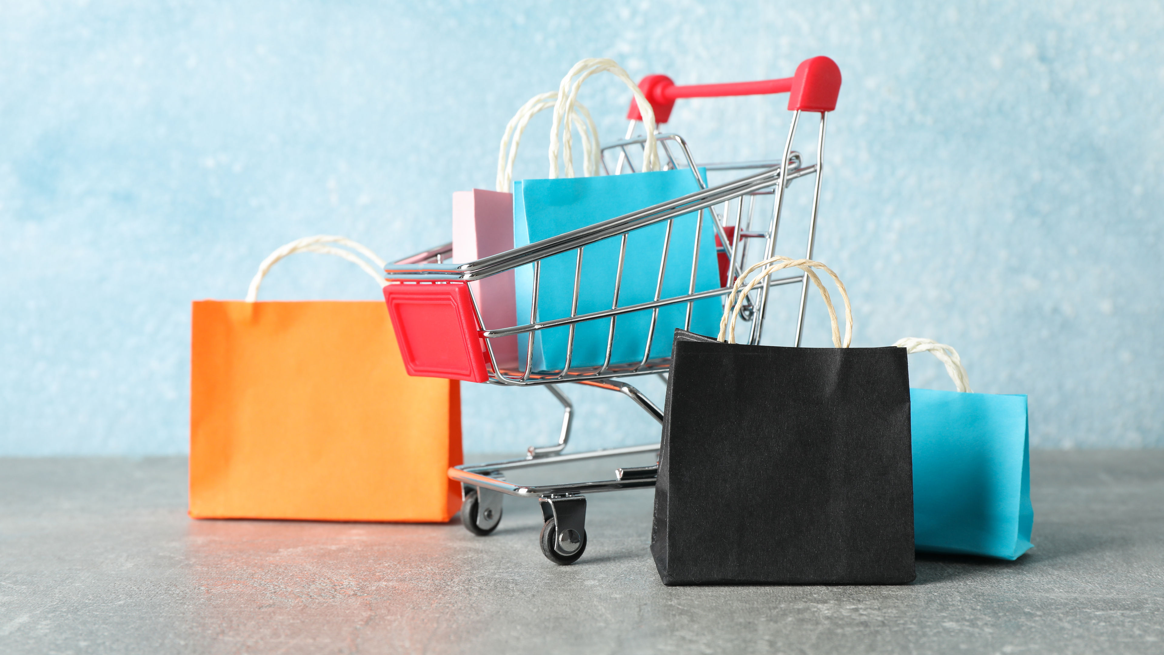 A miniature trolley filled with shopping bags on a light blue background.