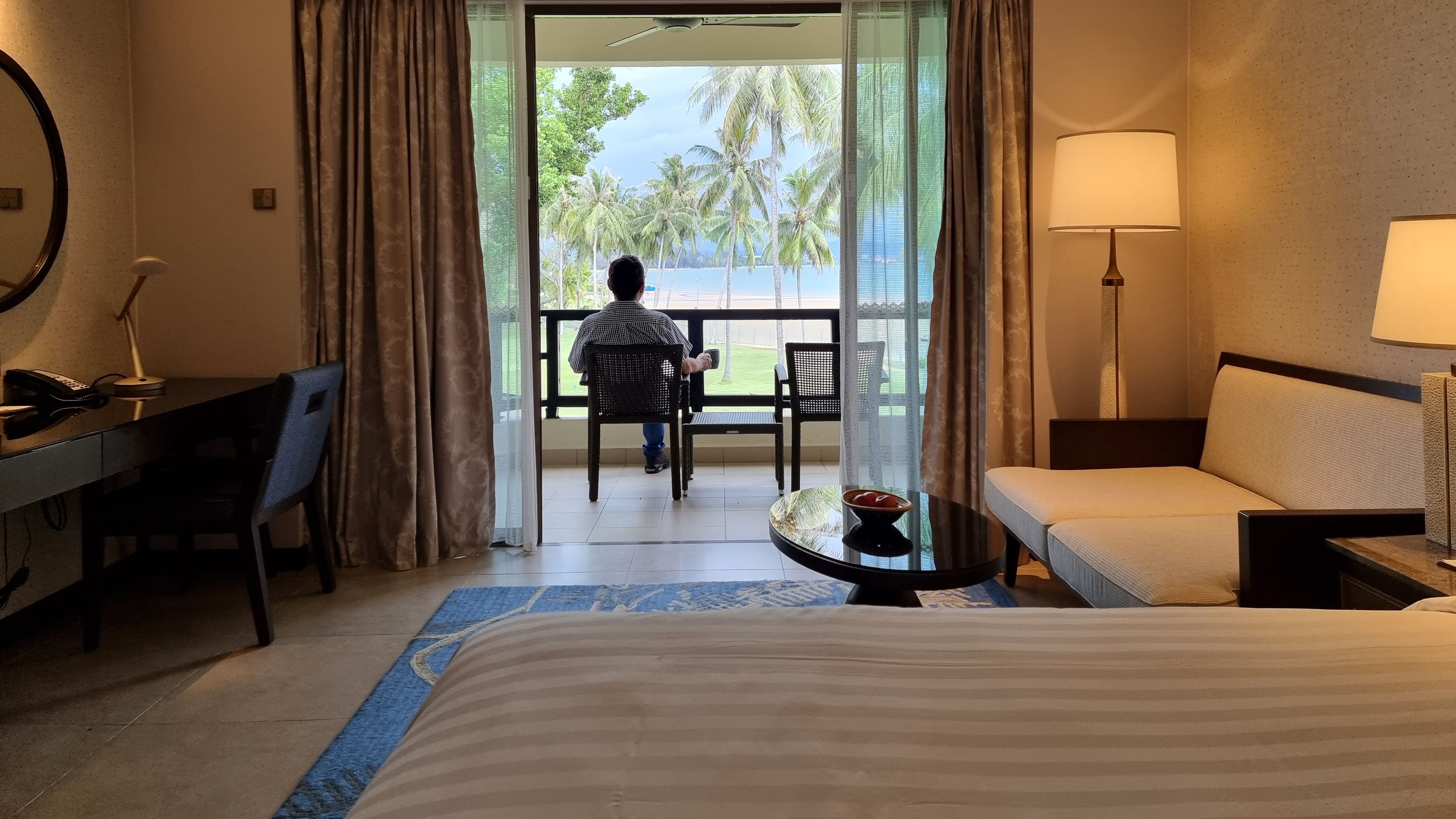 A man seated on a balcony looking at the beach.