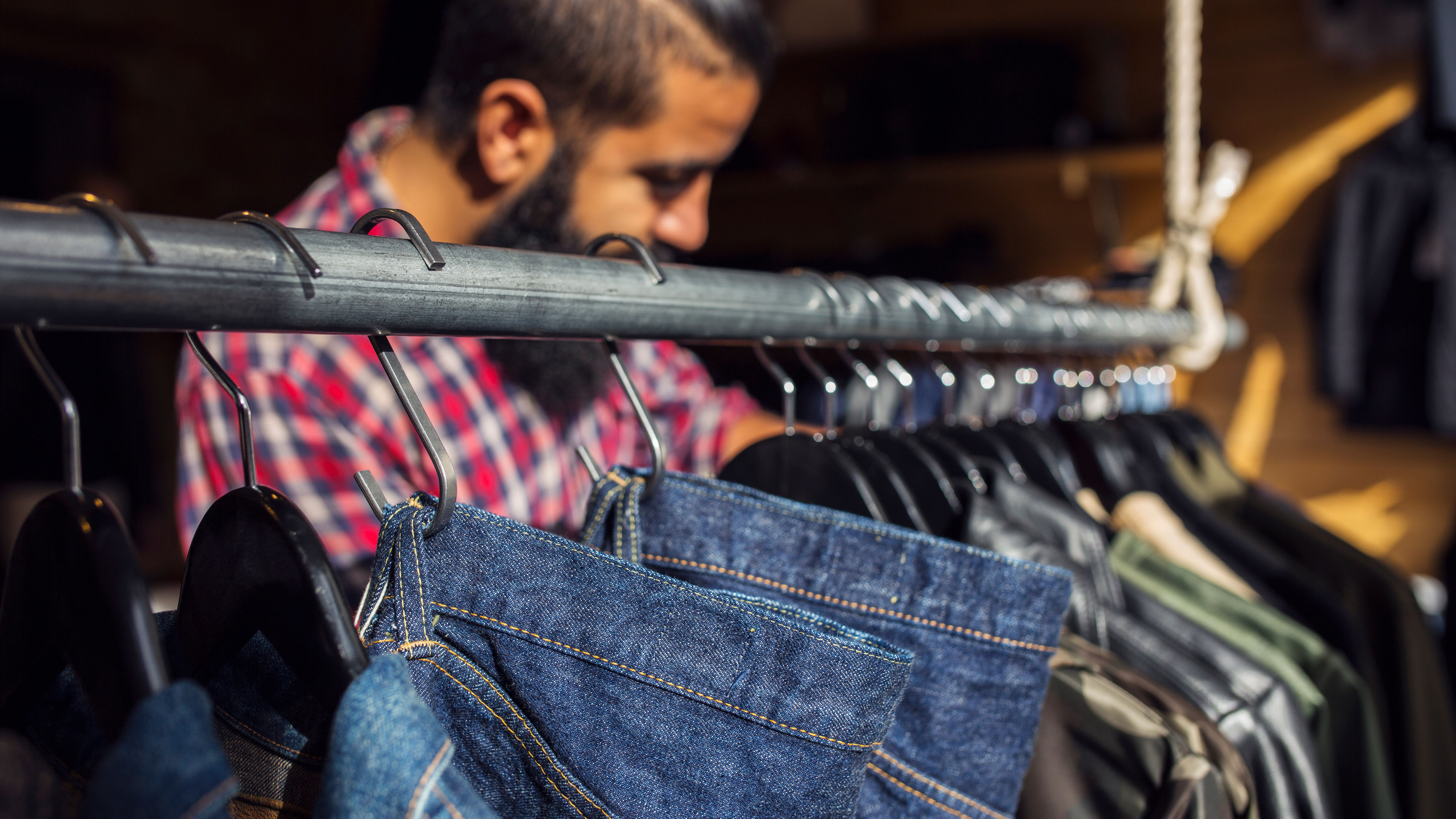 A man browsing through a rack full of jeans, carefully selecting a pair as he shops.