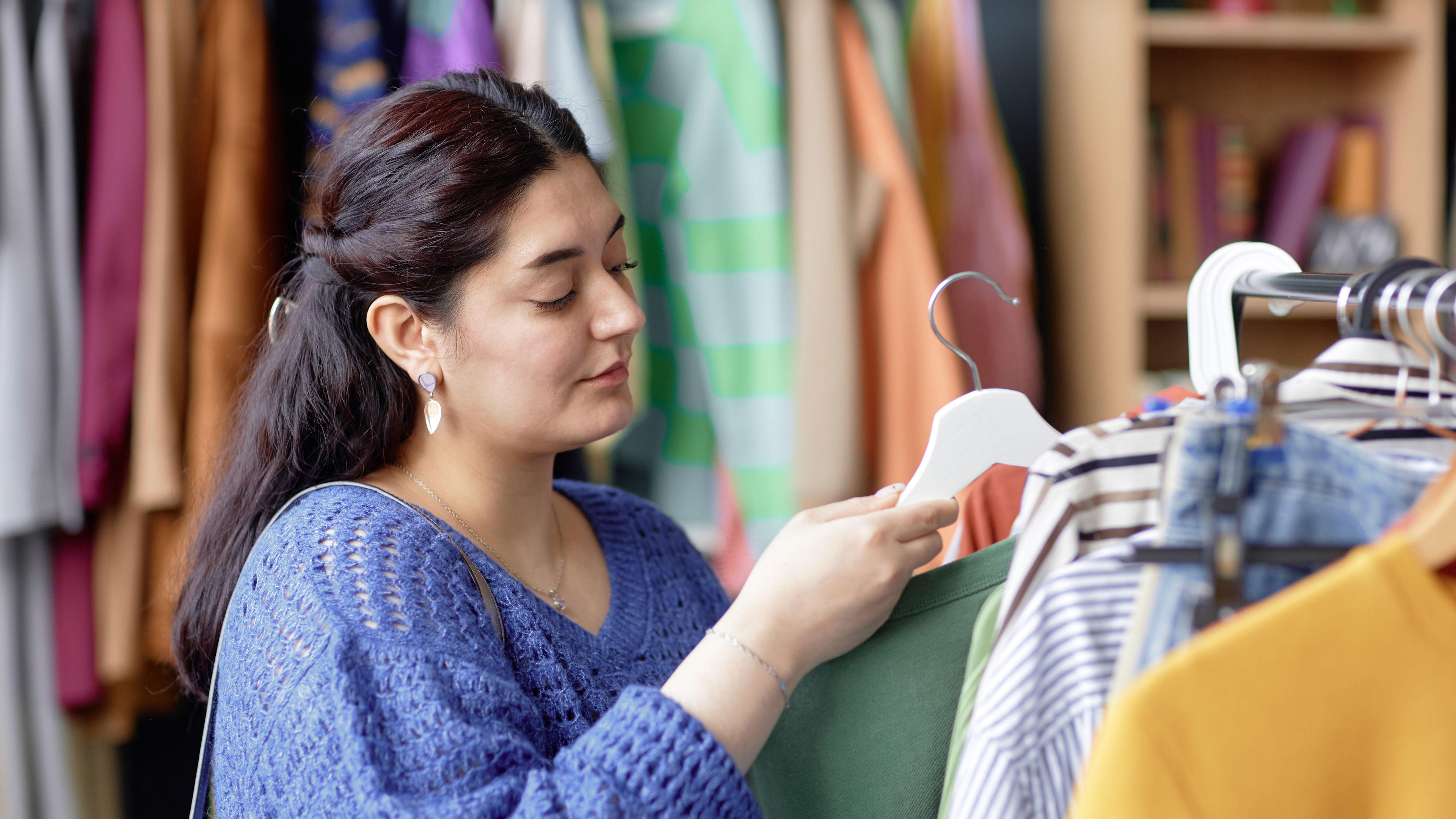 Woman shopping for clothes, examining a green garment on a hanger in a clothing store.






