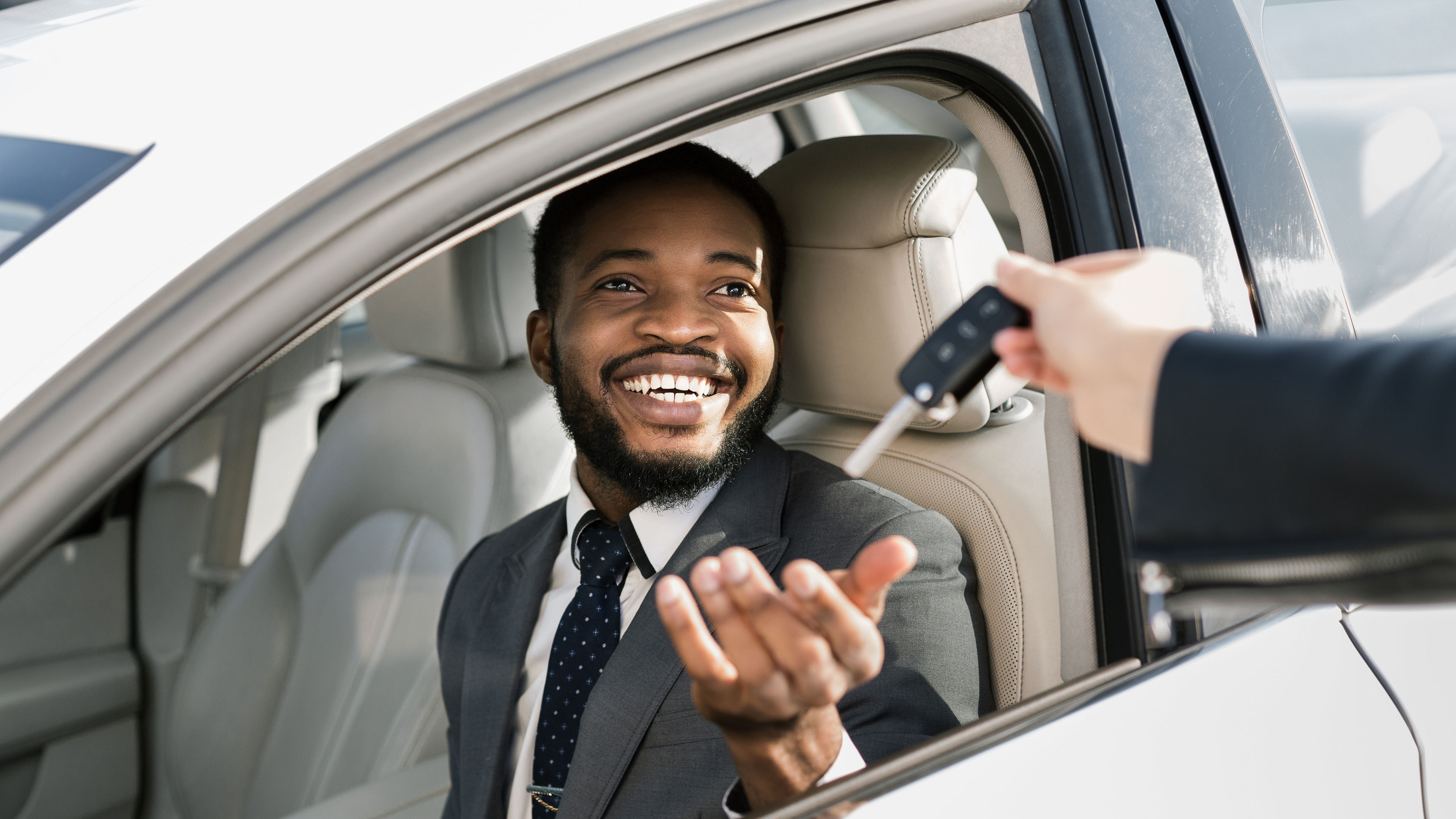 A car key is handed over to a African American man in a car.