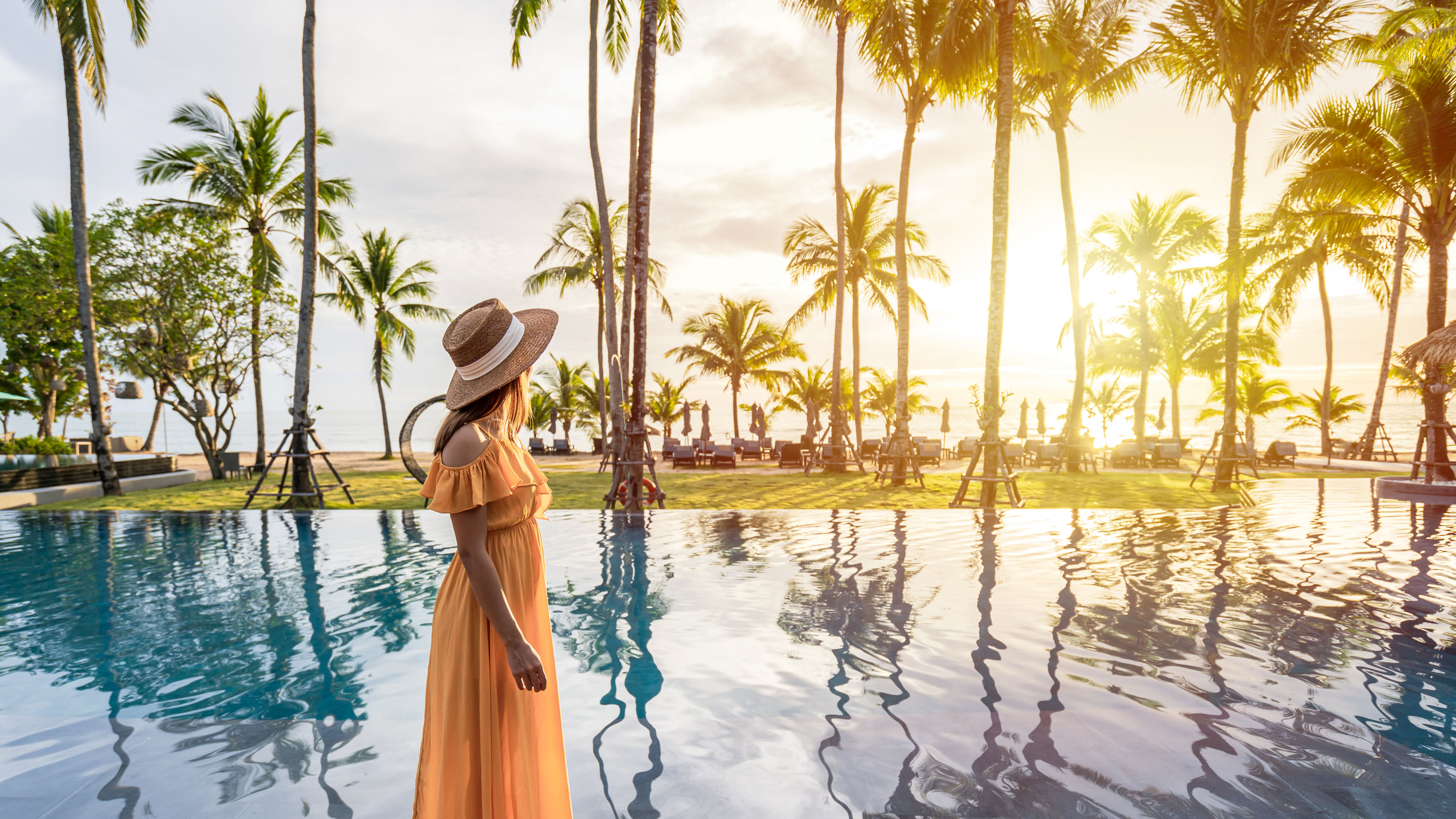 A young woman traveler with a hat enjoying the sunset by a poolside.