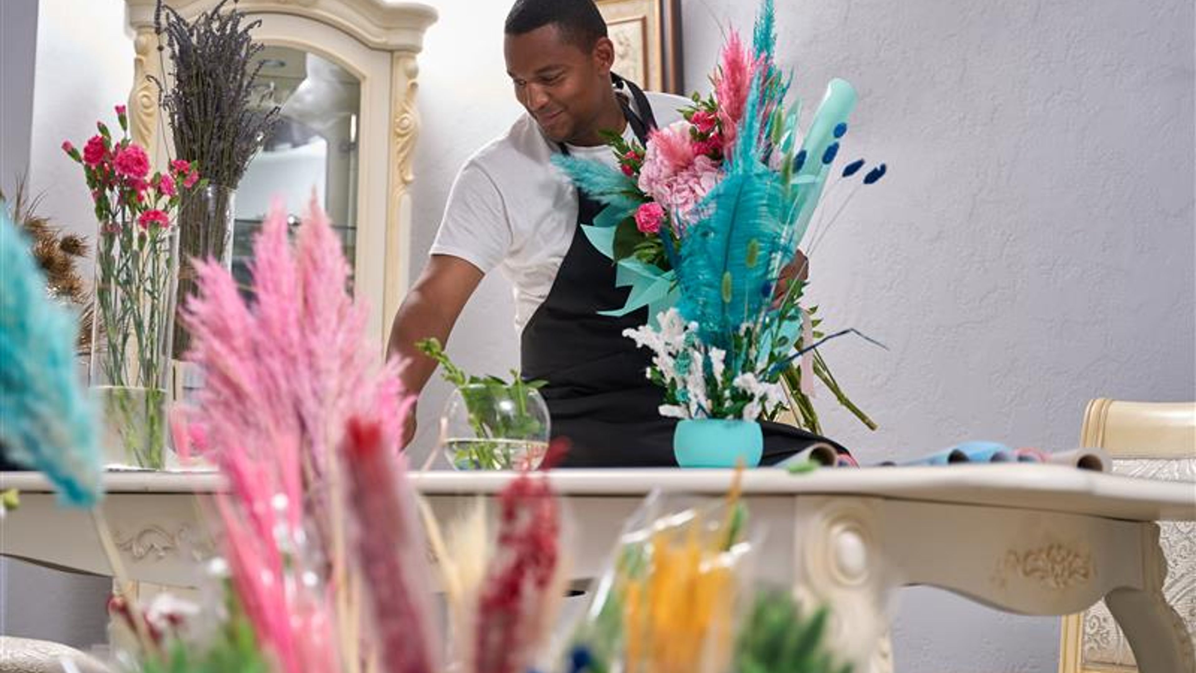 A cheerful florist is holding a fresh bouquet while standing in front of a decorated table.