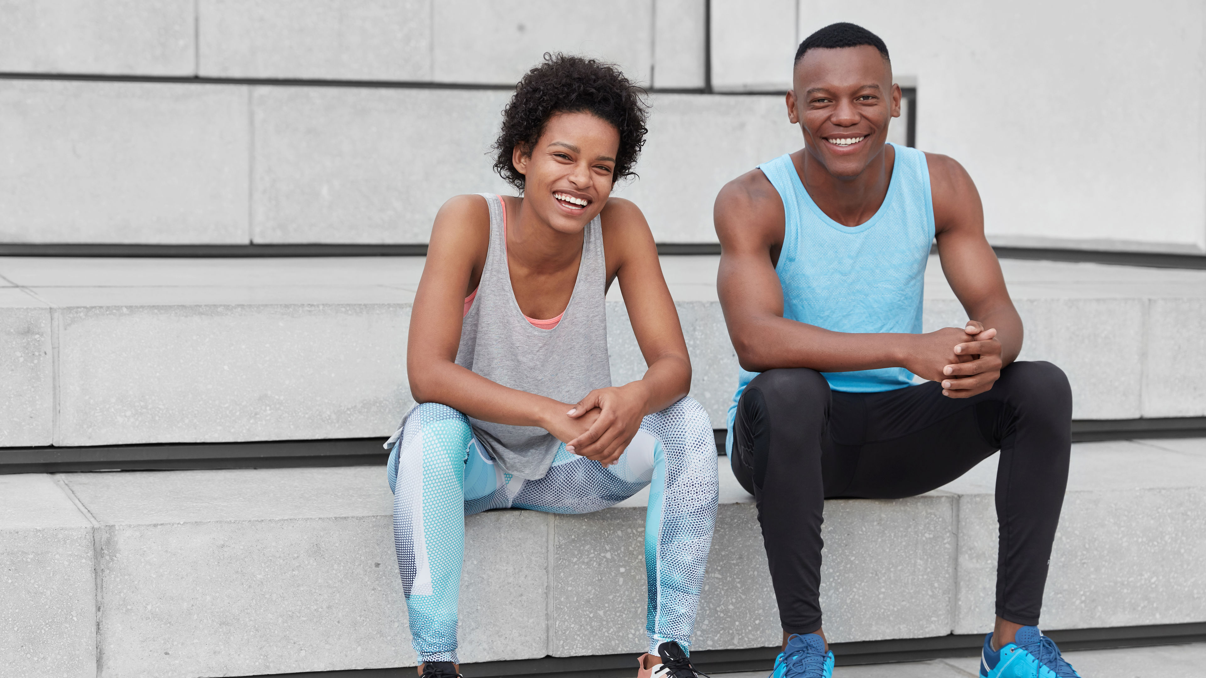 Shot of relaxed African woman and man with positive expressions, dressed in sports wear.