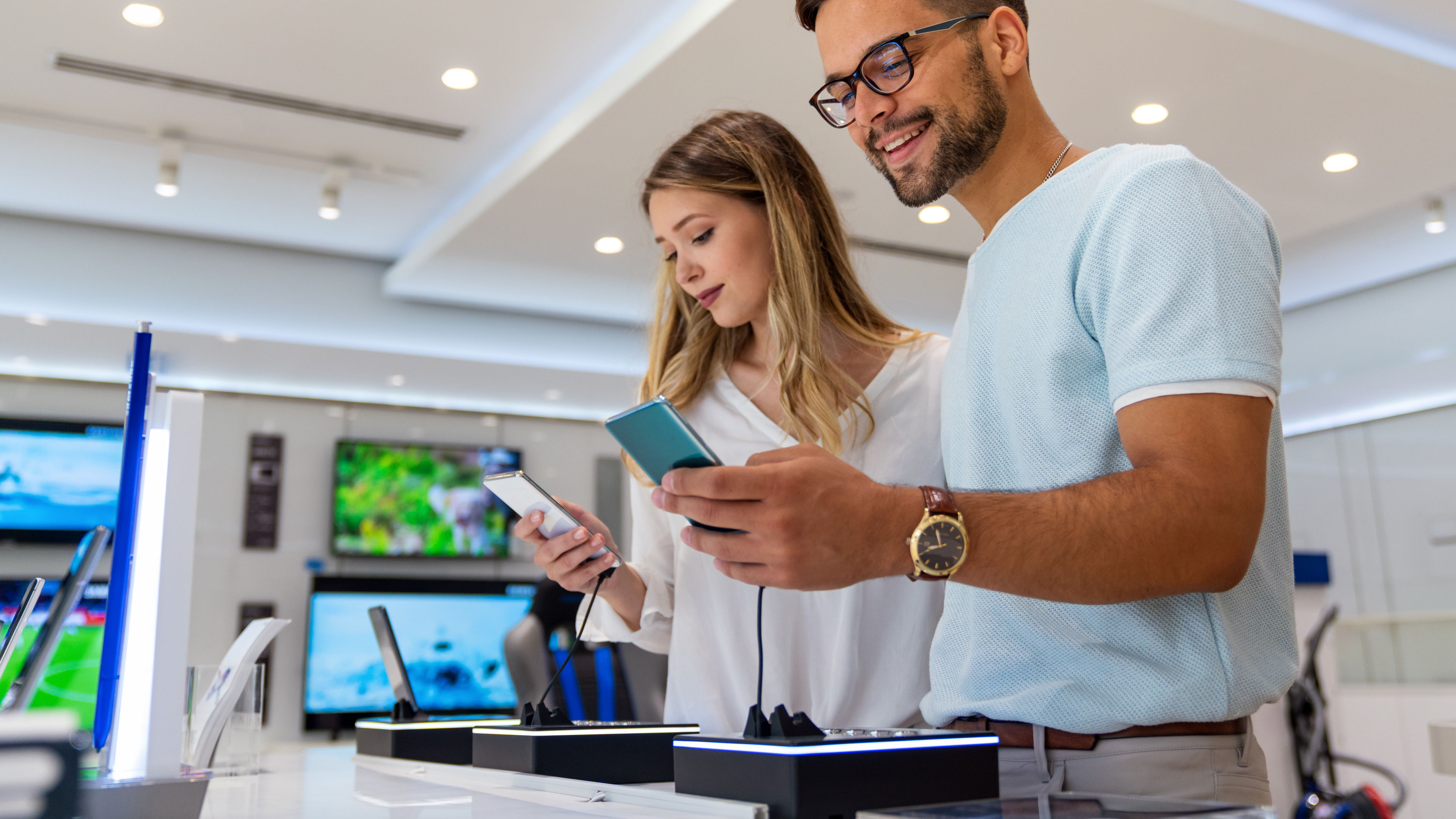 Young couple in blue and white shopping for new smartphones in a gadget store.