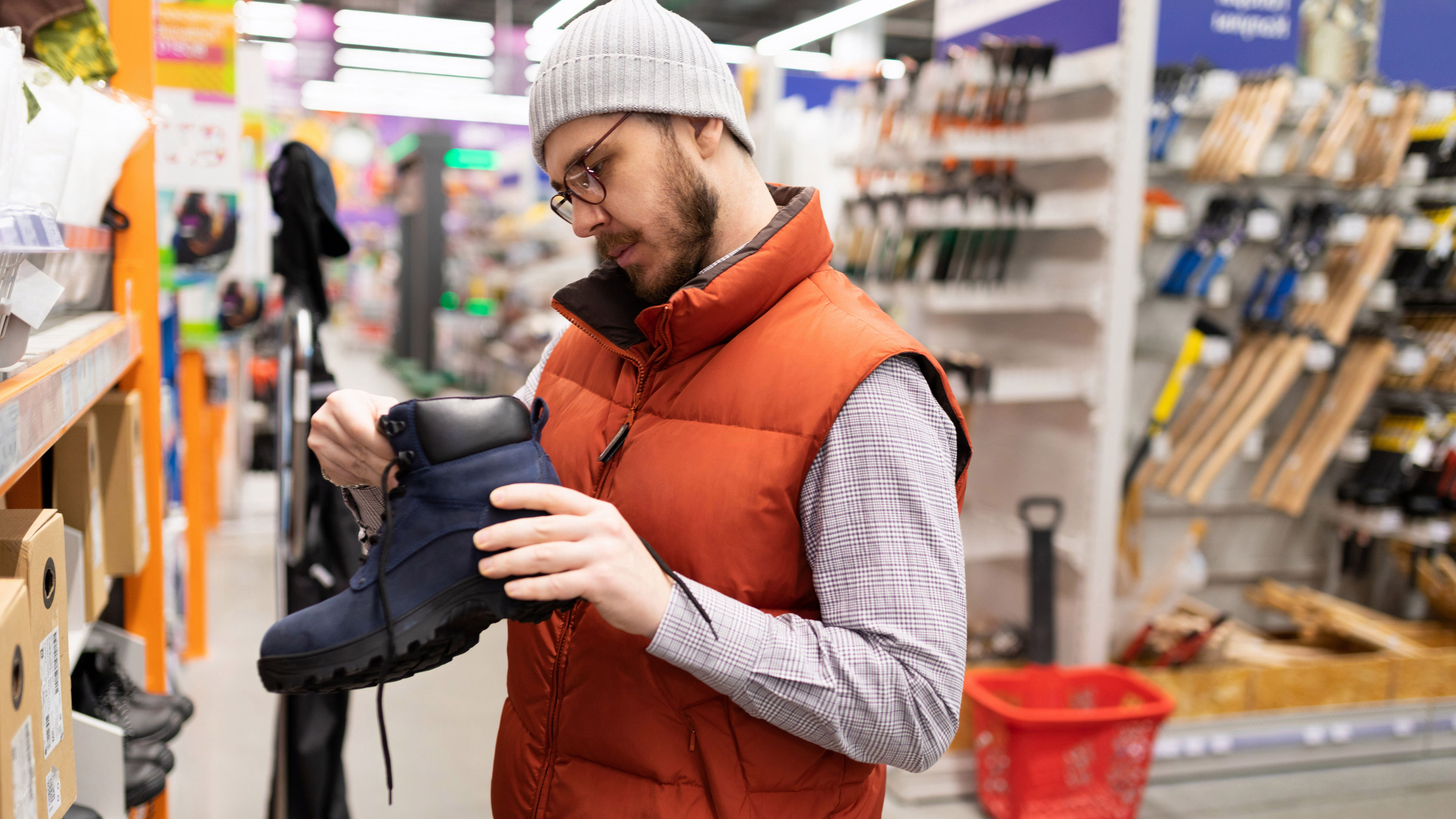 A man wearing an orange jacket examining construction boots in a store.