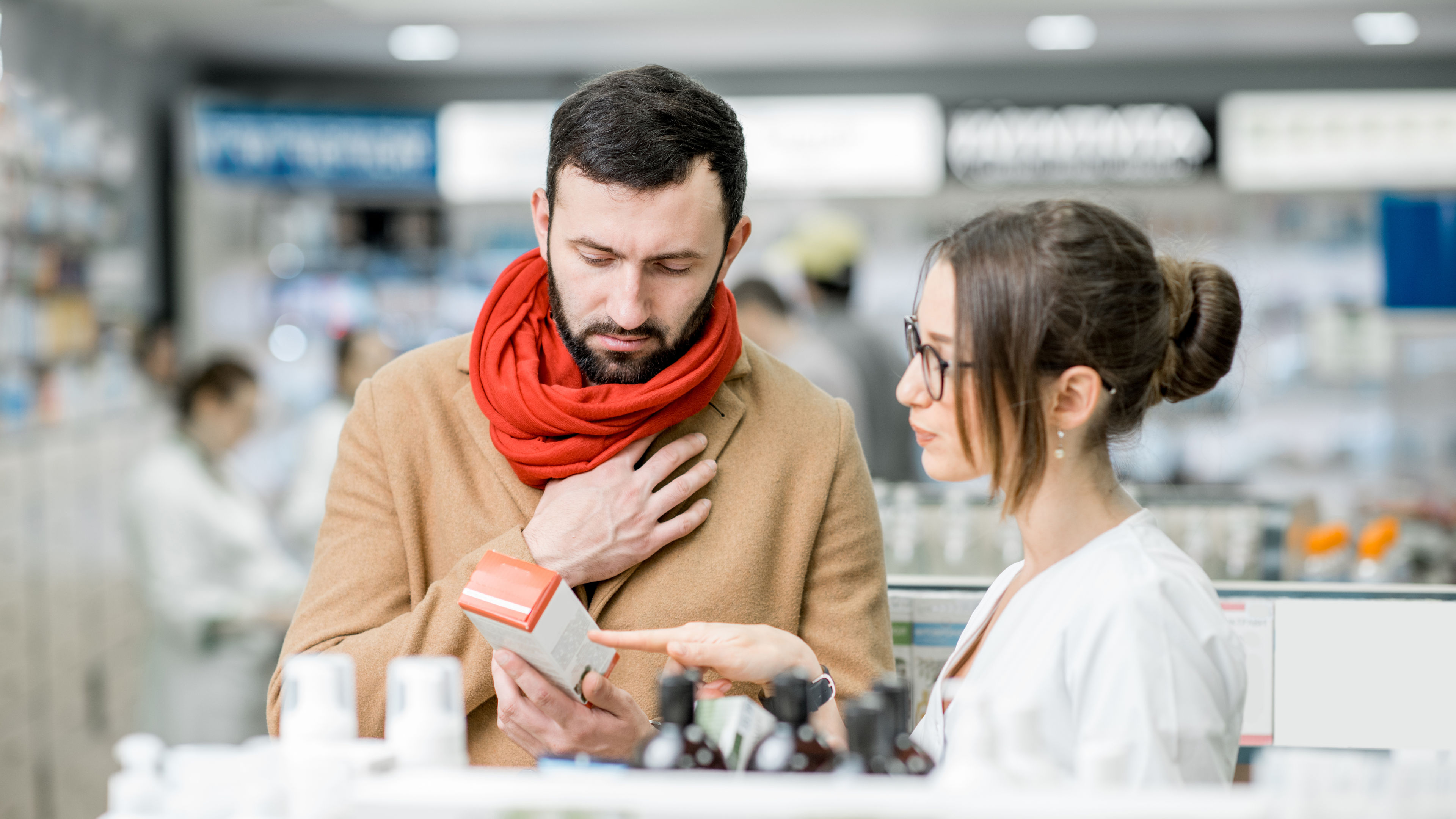 A pharmacist explaining a product to a client inside a pharmacy store.